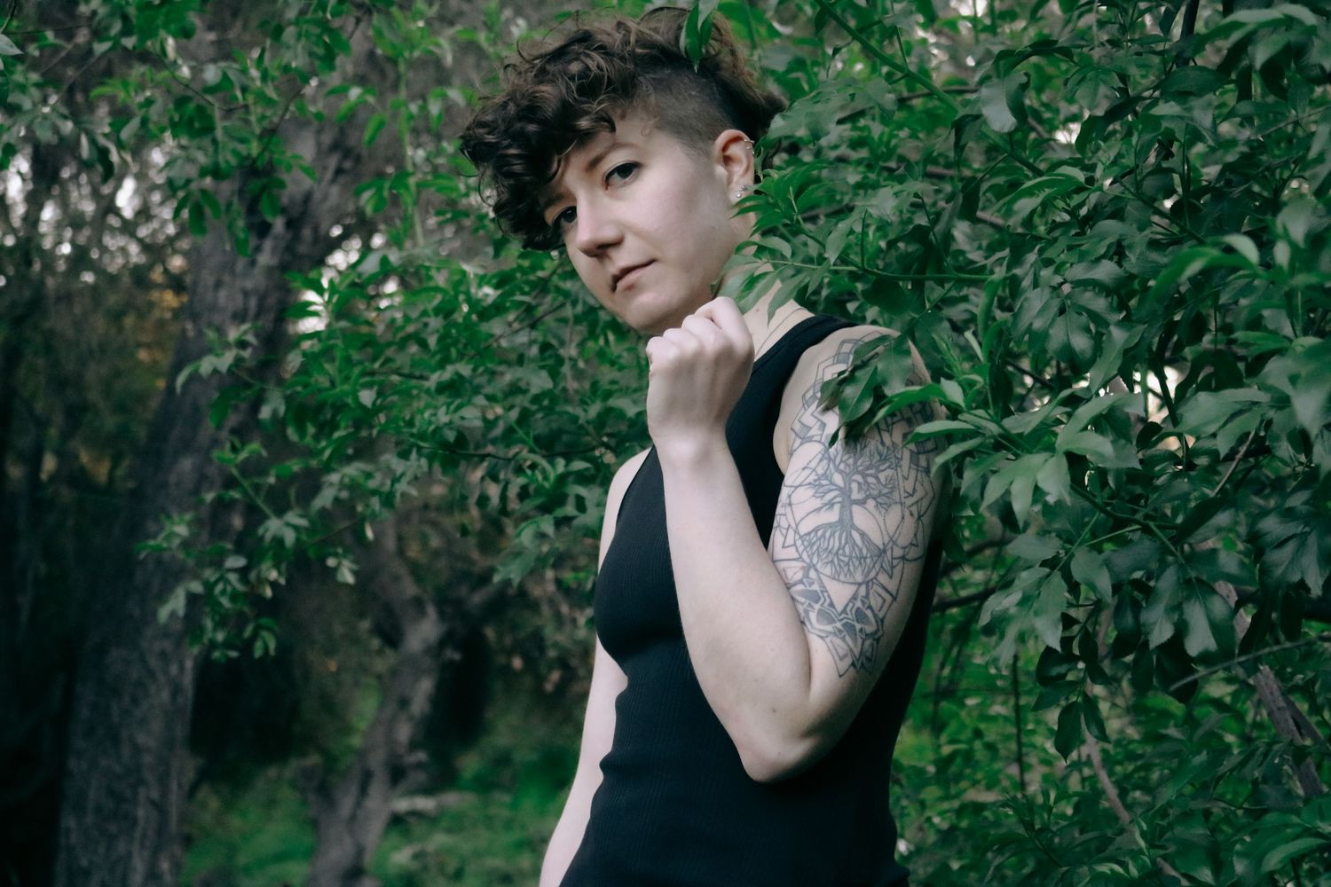 Ethereal portrait in nature showing person in black top with detailed sleeve tattoo.