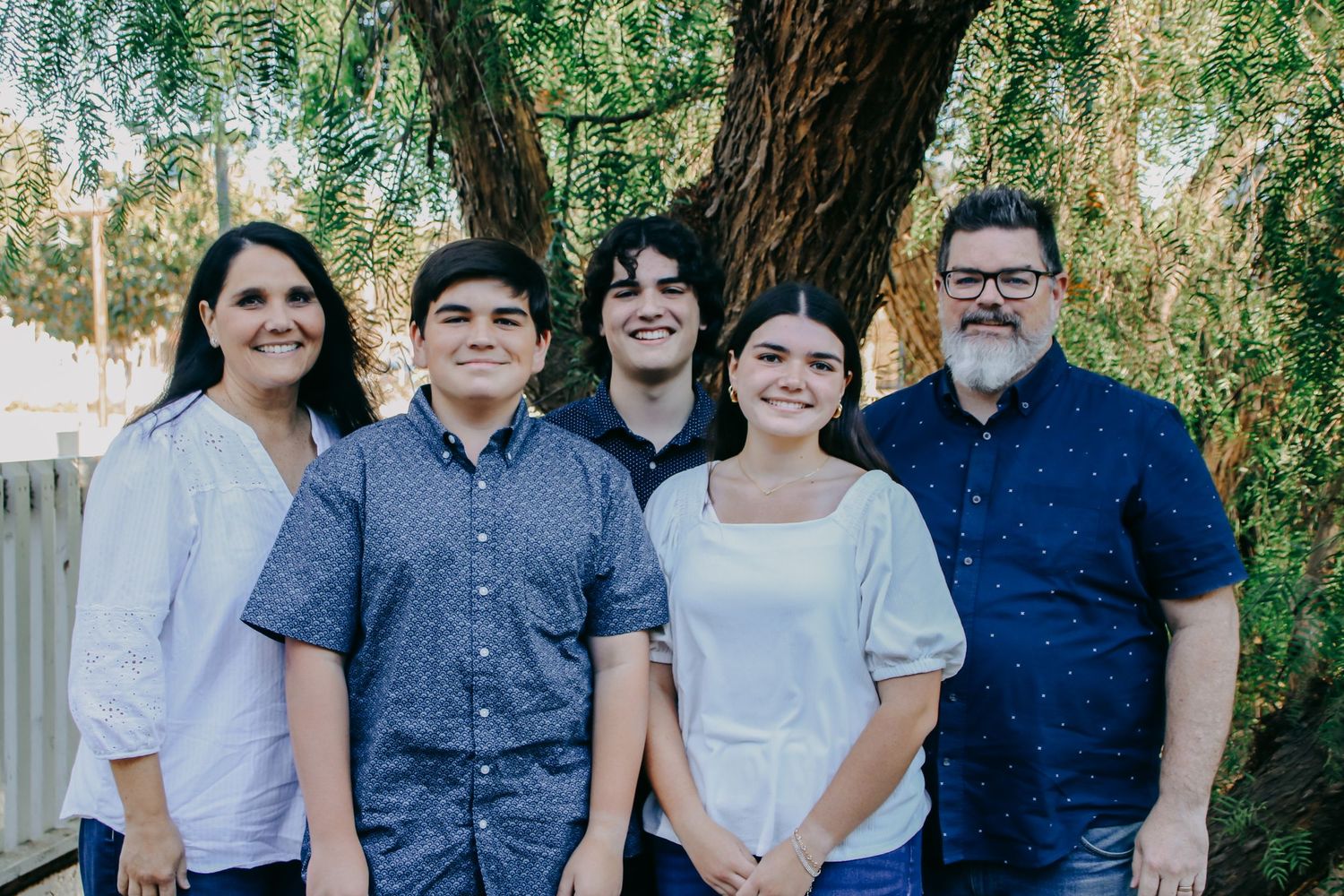 Color portrait of smiling family members in coordinated blue and white outfits under tree.