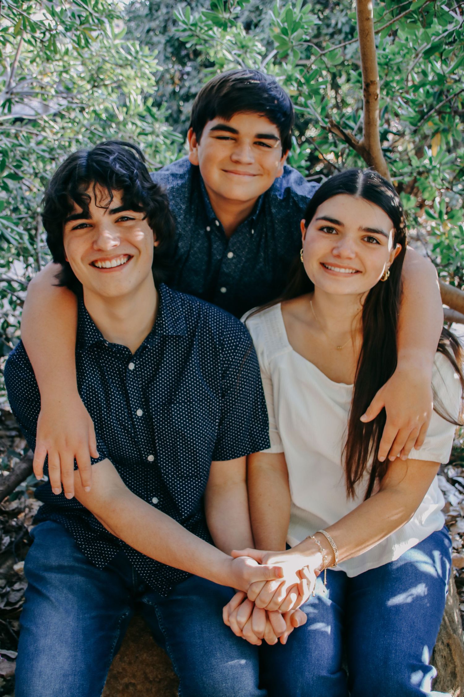Three people sharing candid moments together while sitting outdoors under trees.