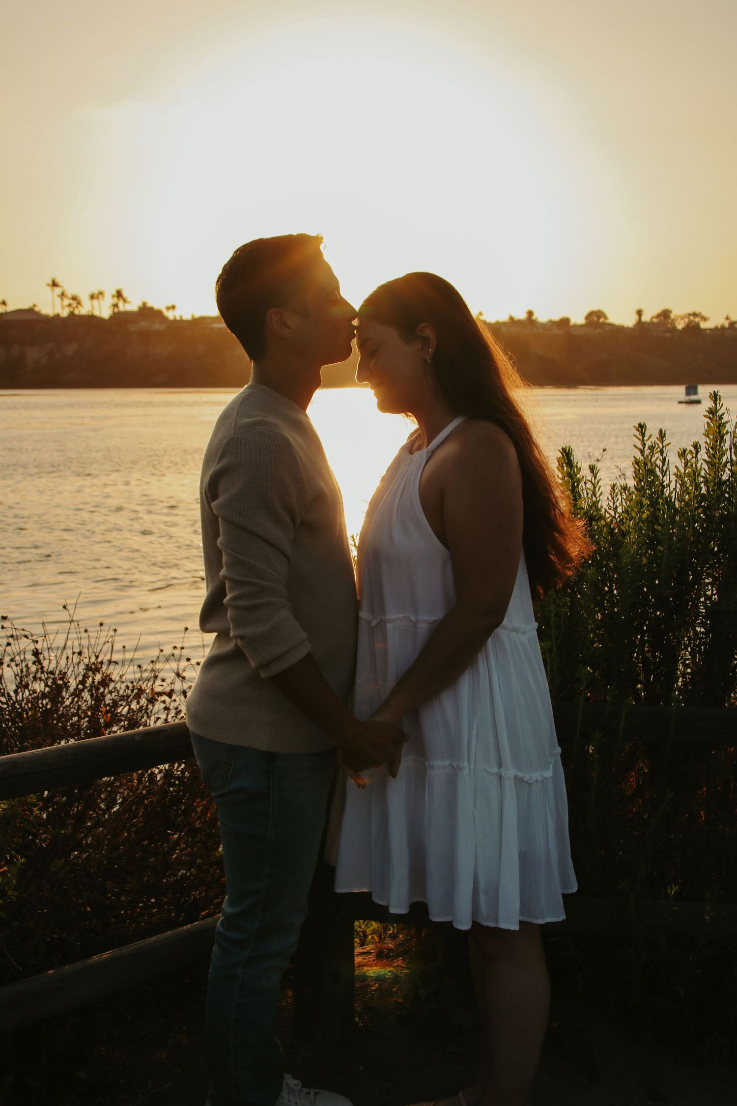 Silhouetted couple in romantic pose against sunset over water landscape.