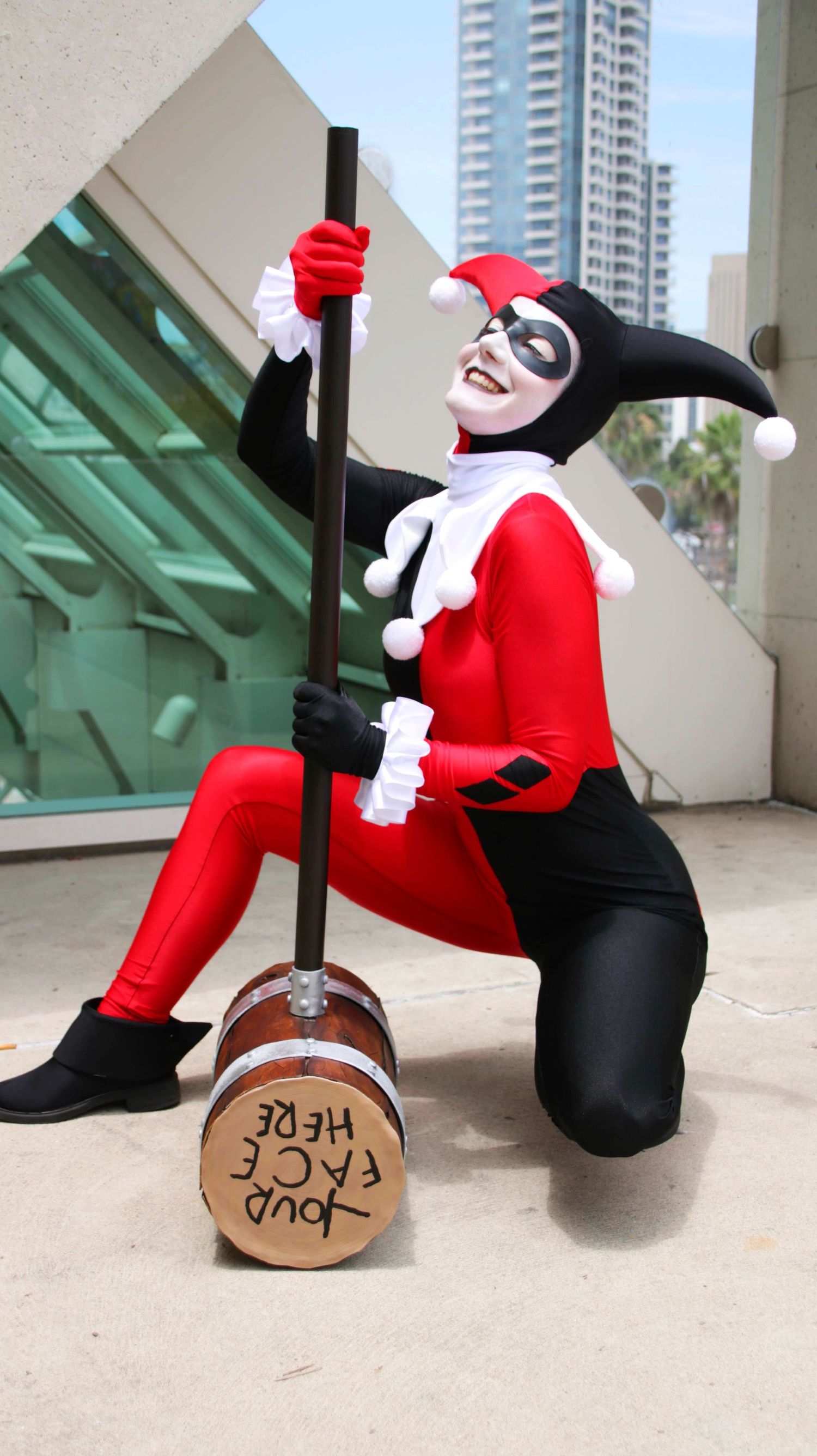 Cosplayer dressed as Harley Quinn poses playfully with a large mallet prop.