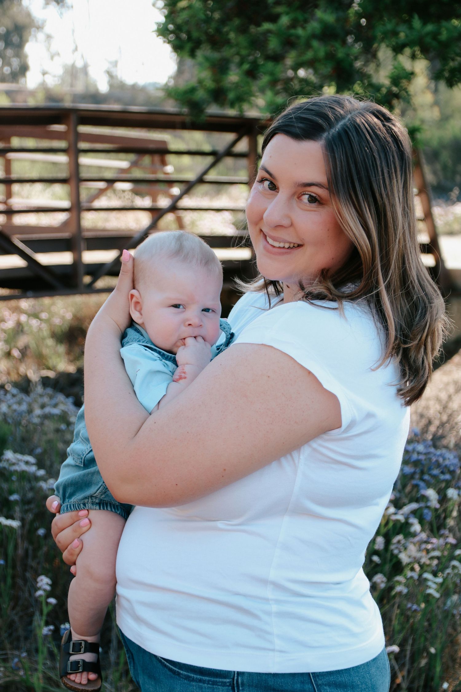 Tender moment between parent and baby outdoors with rustic fence and wildflowers.