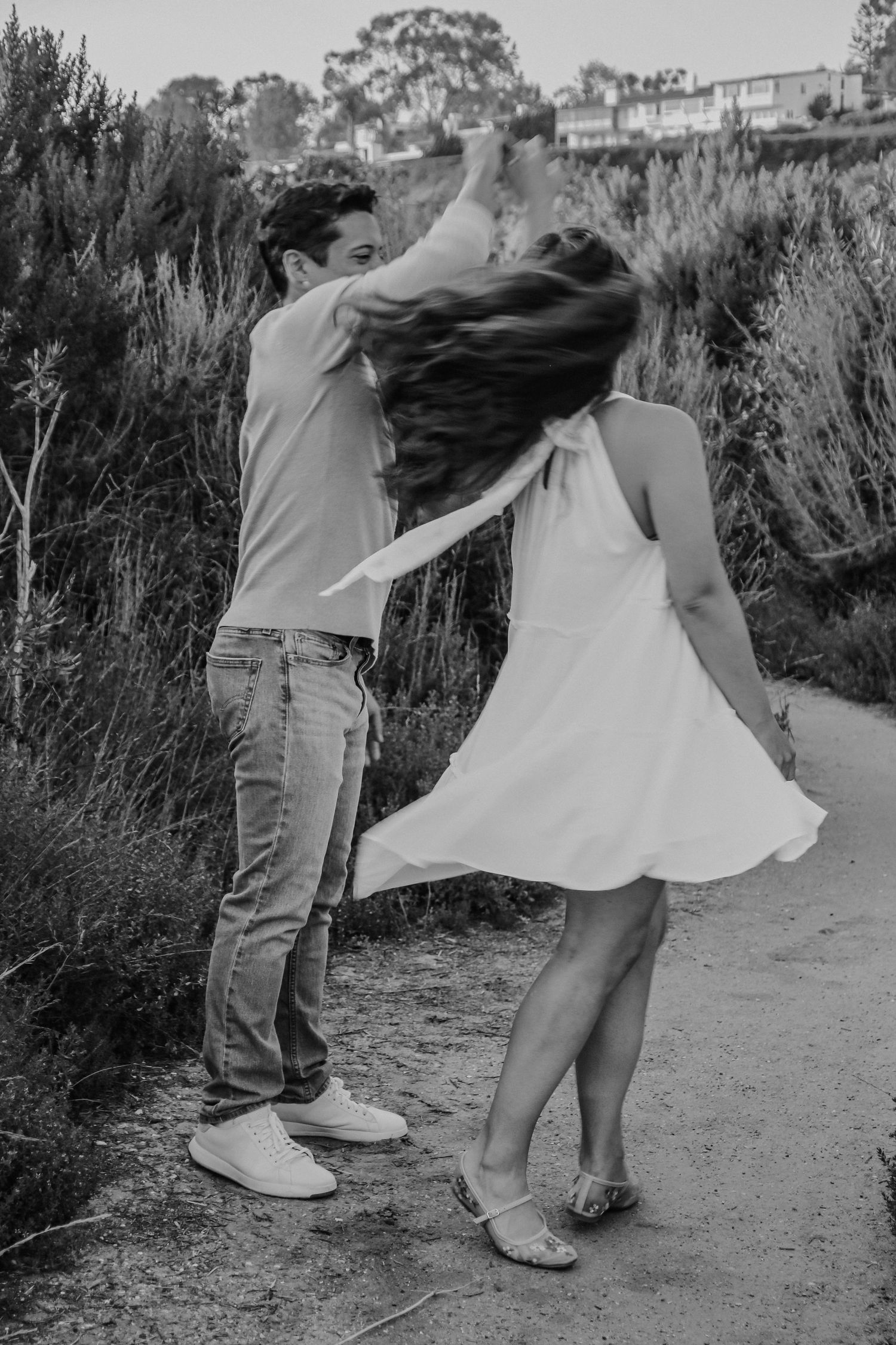 A couple spins and dances together on a scenic coastal path, captured in black and white.