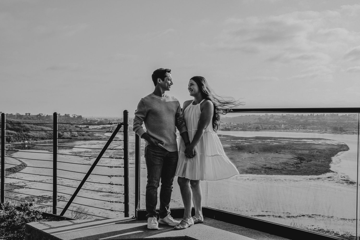 A couple shares a quiet moment together on a viewing platform overlooking a coastal landscape.