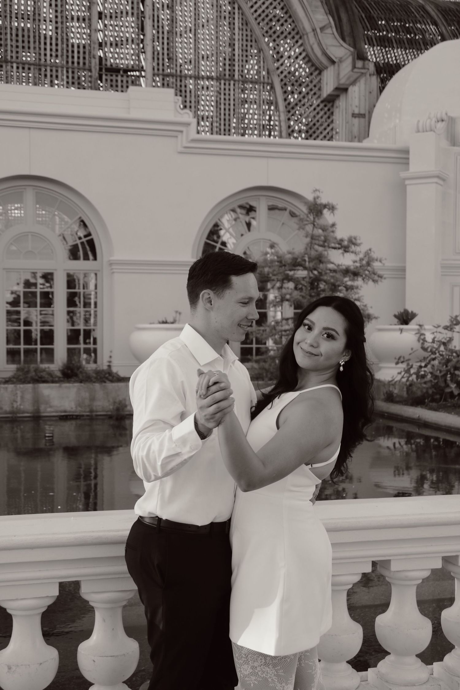 A couple shares an intimate dance moment by a classical architectural setting in black and white.