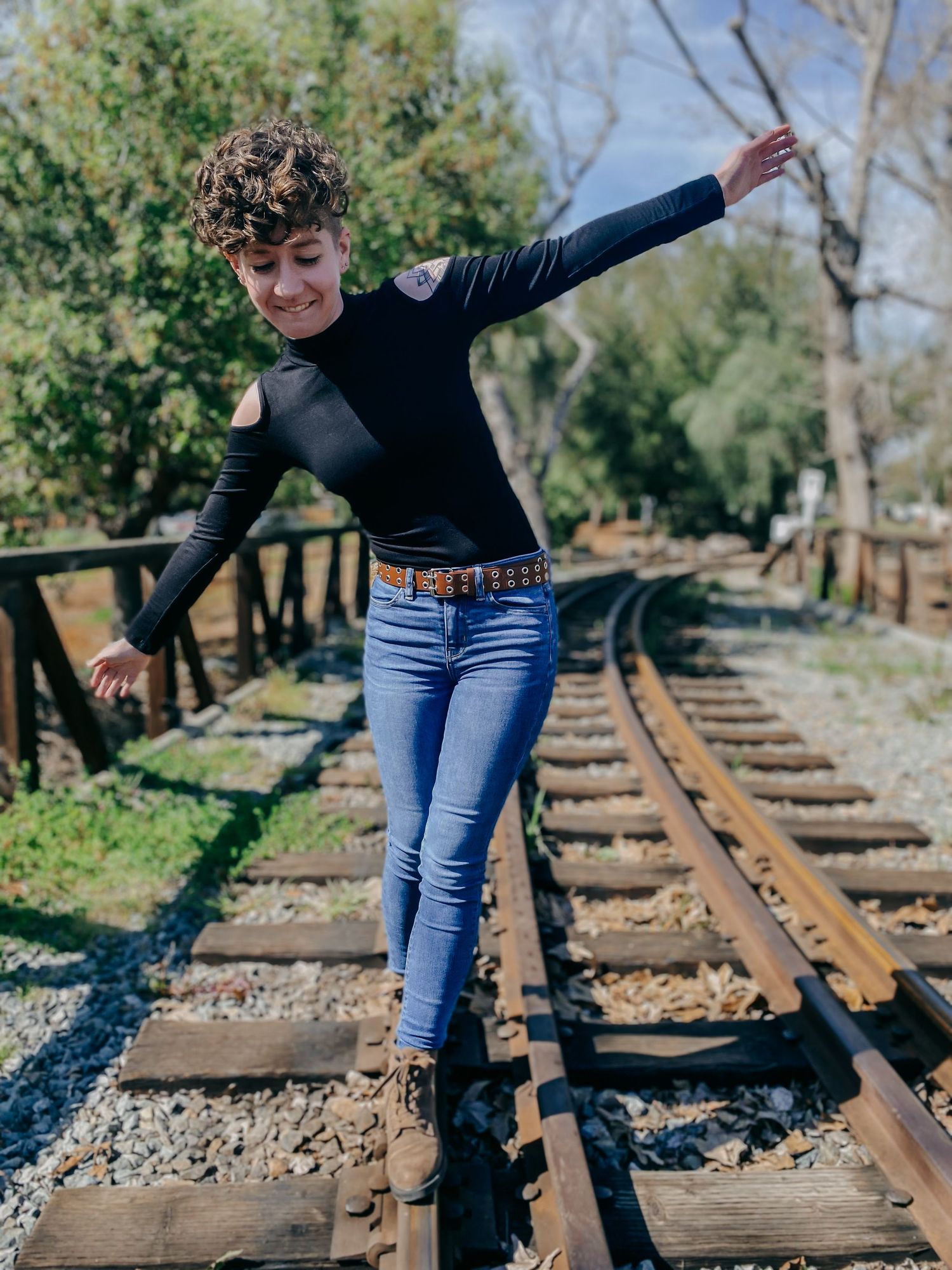 Figure practicing balance exercises on rustic railroad tracks surrounded by trees and foliage.