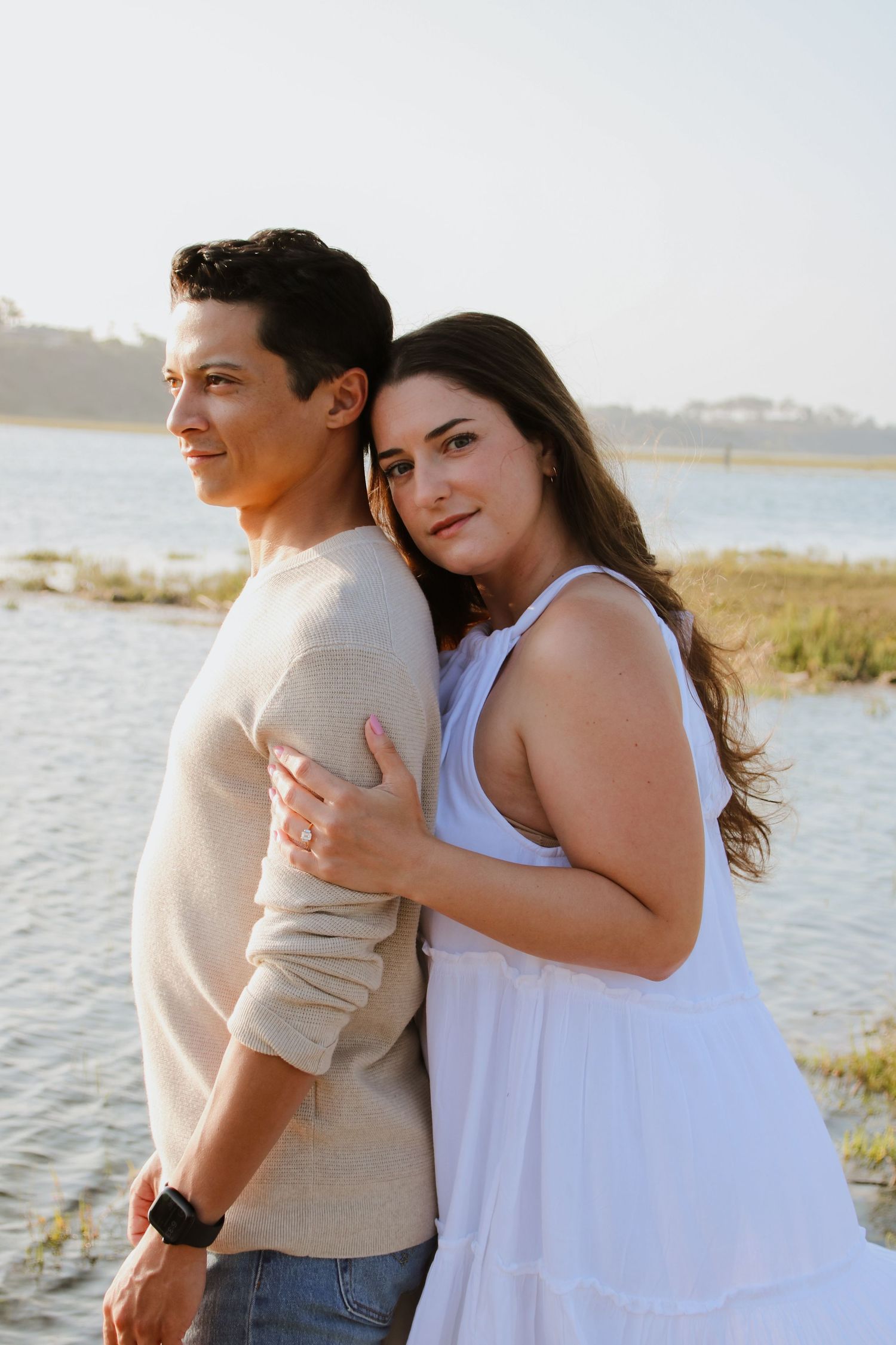 Happy couple posing together in casual attire against a waterfront landscape.