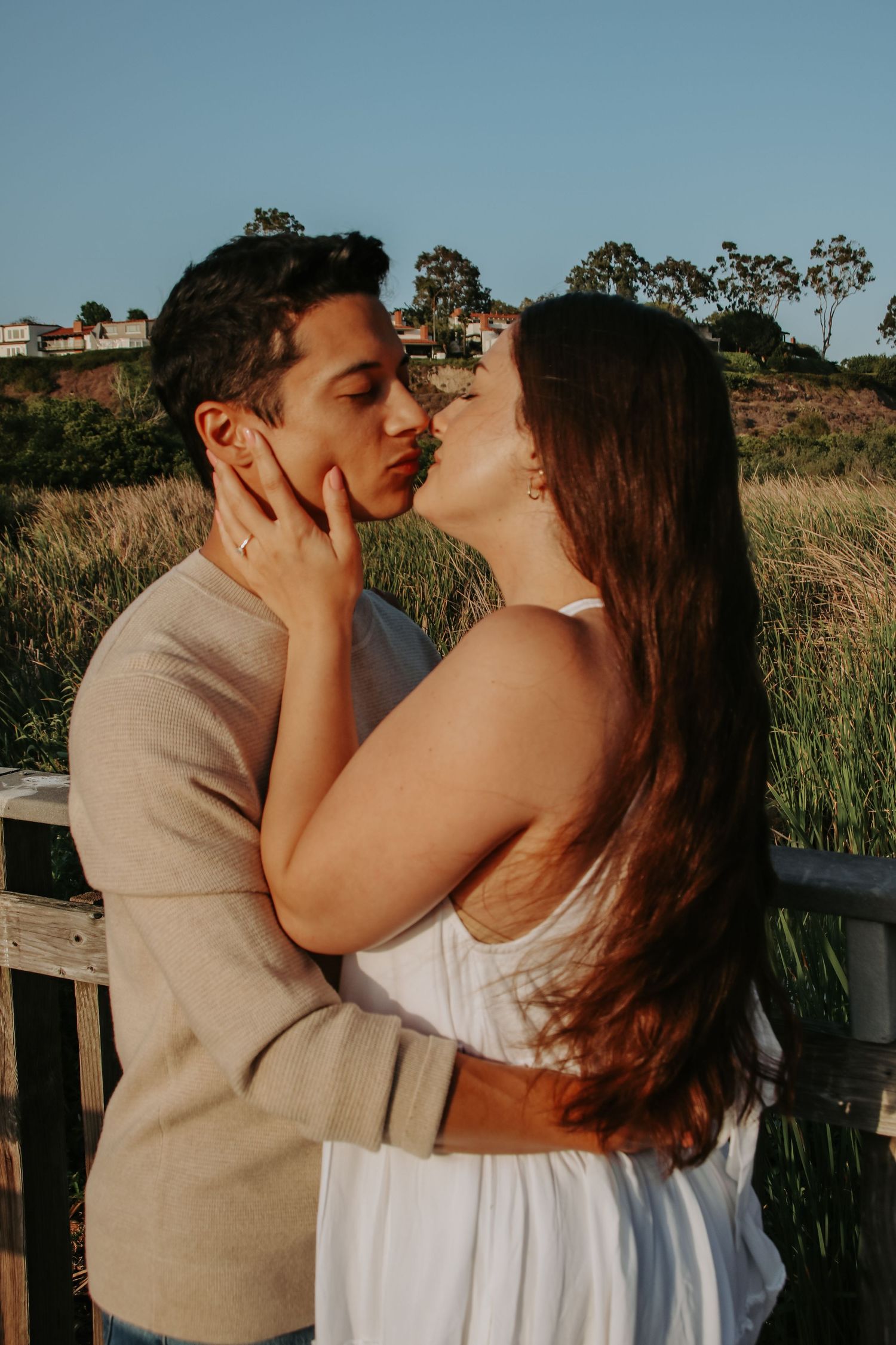Sunset portrait of couple in white dress and beige sweater sharing romantic moment outdoors.
