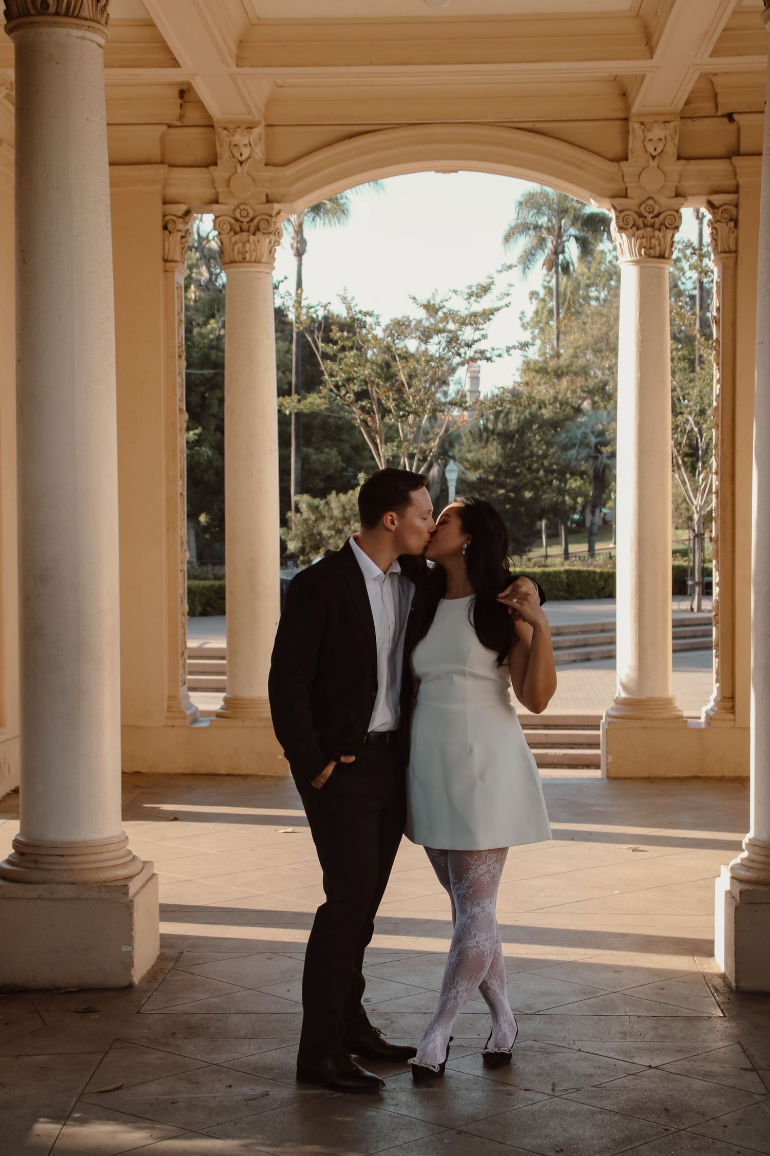 A romantic moment captured between two people in a pillared corridor with afternoon light.