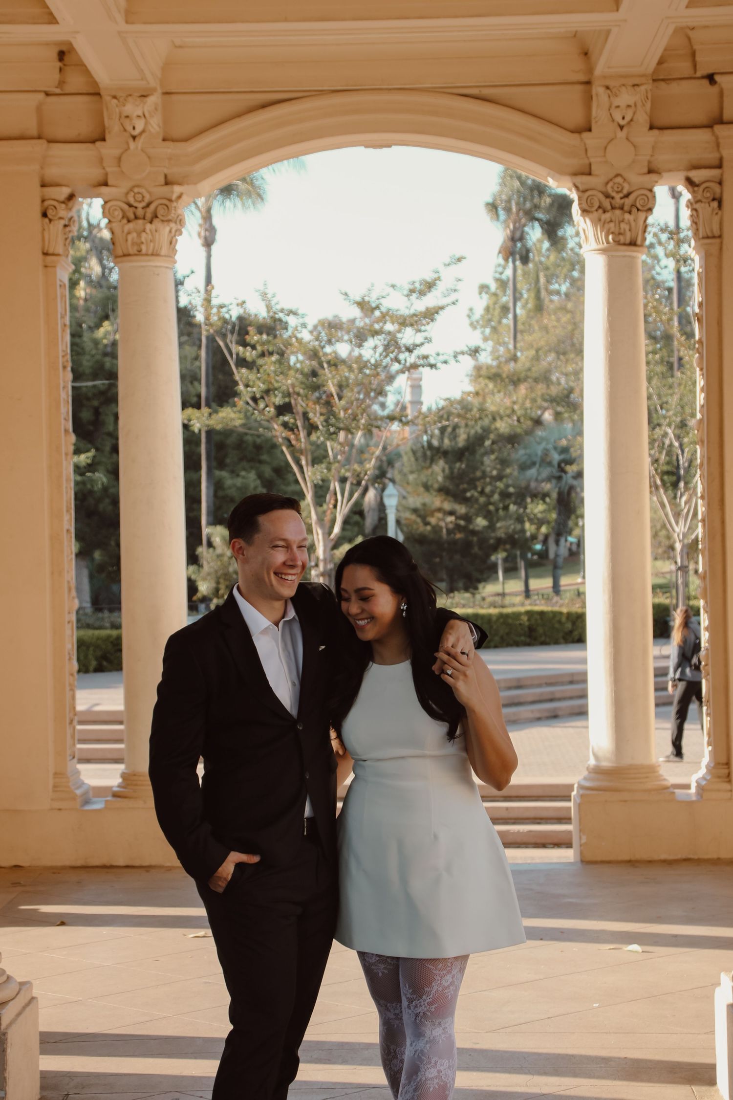 Two people share laughter while posing against classical columns in warm afternoon light.