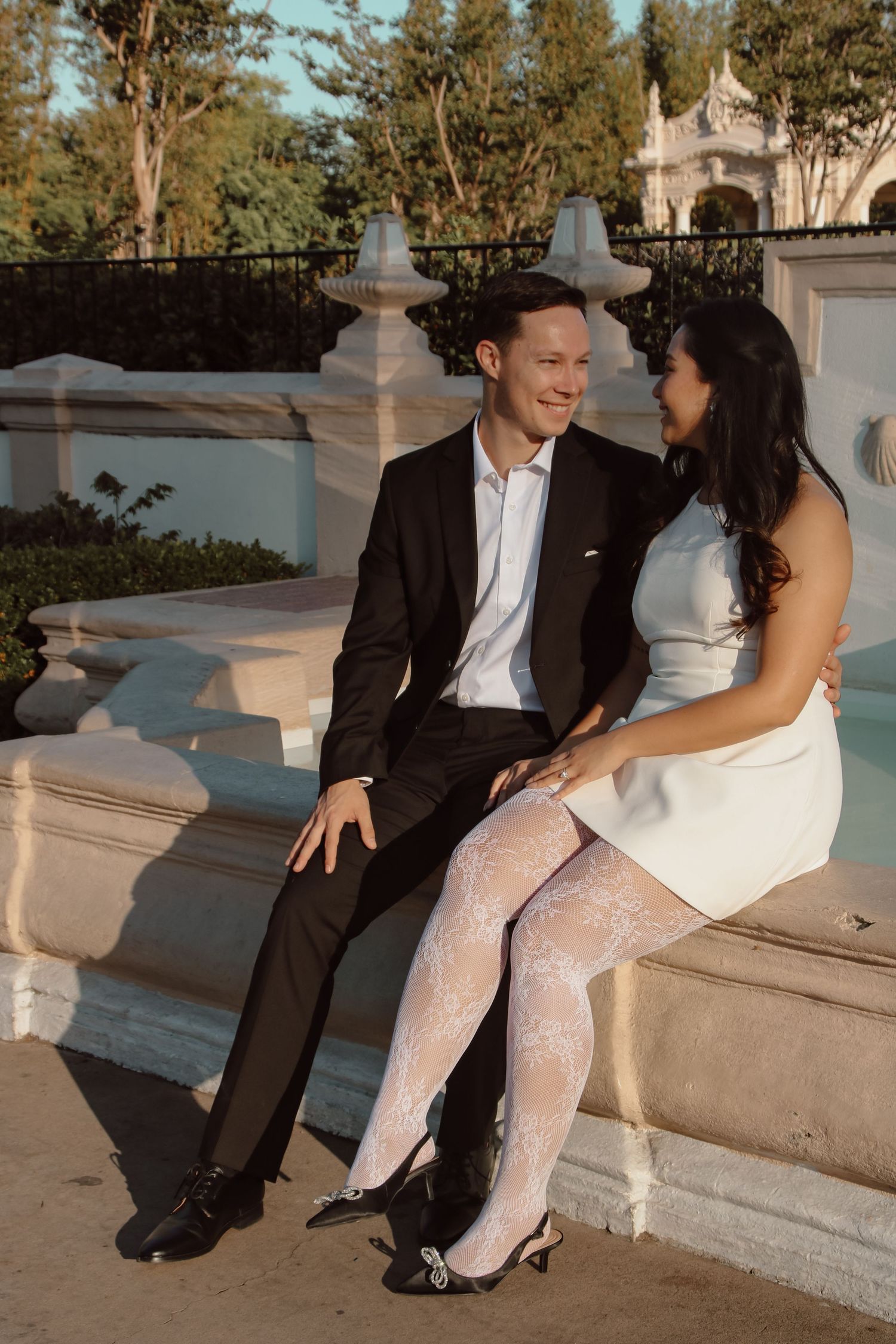 Romantic couple in formal wear sitting together on ornate stone steps during golden hour.