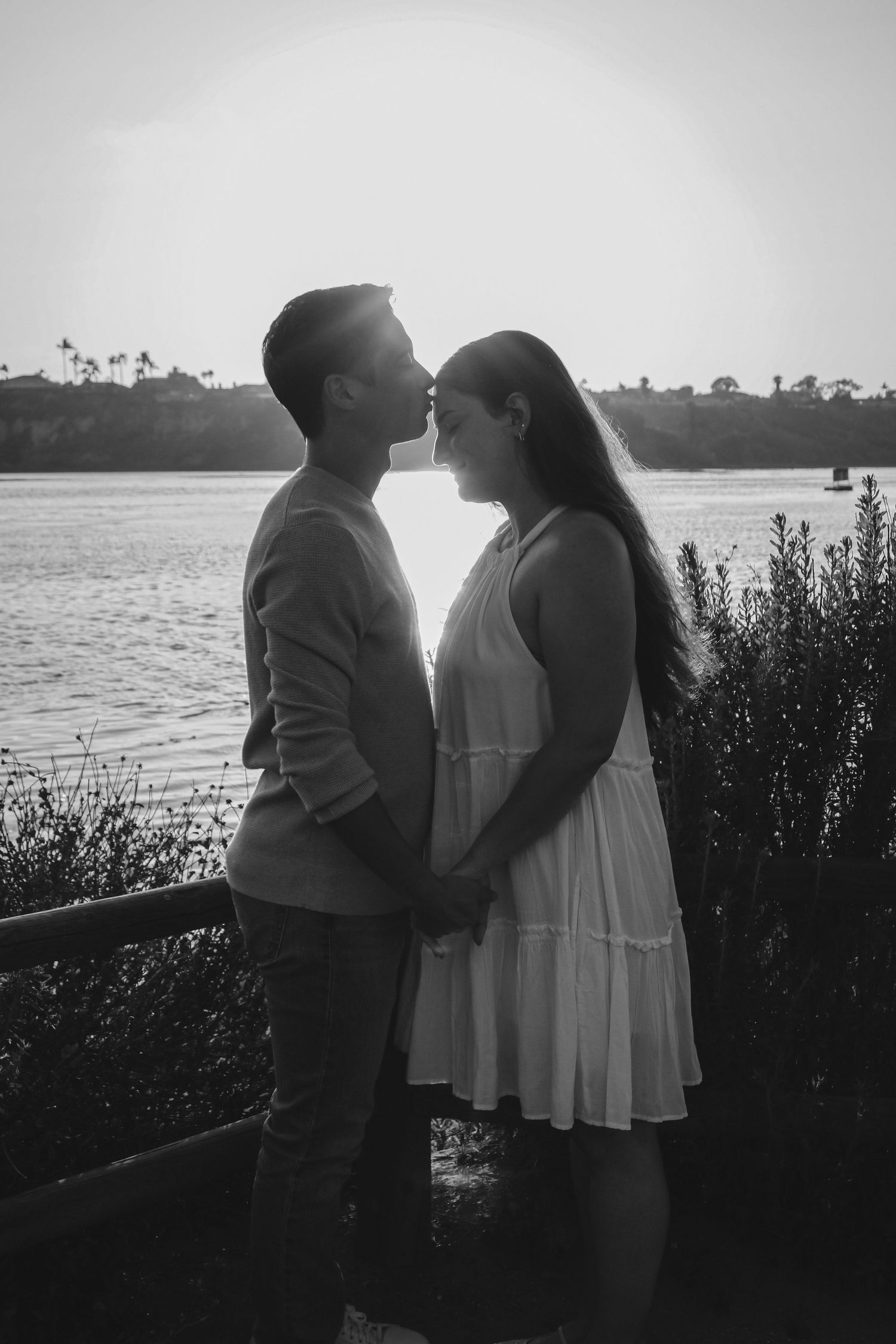 Black and white portrait of couple in intimate moment against water backdrop.