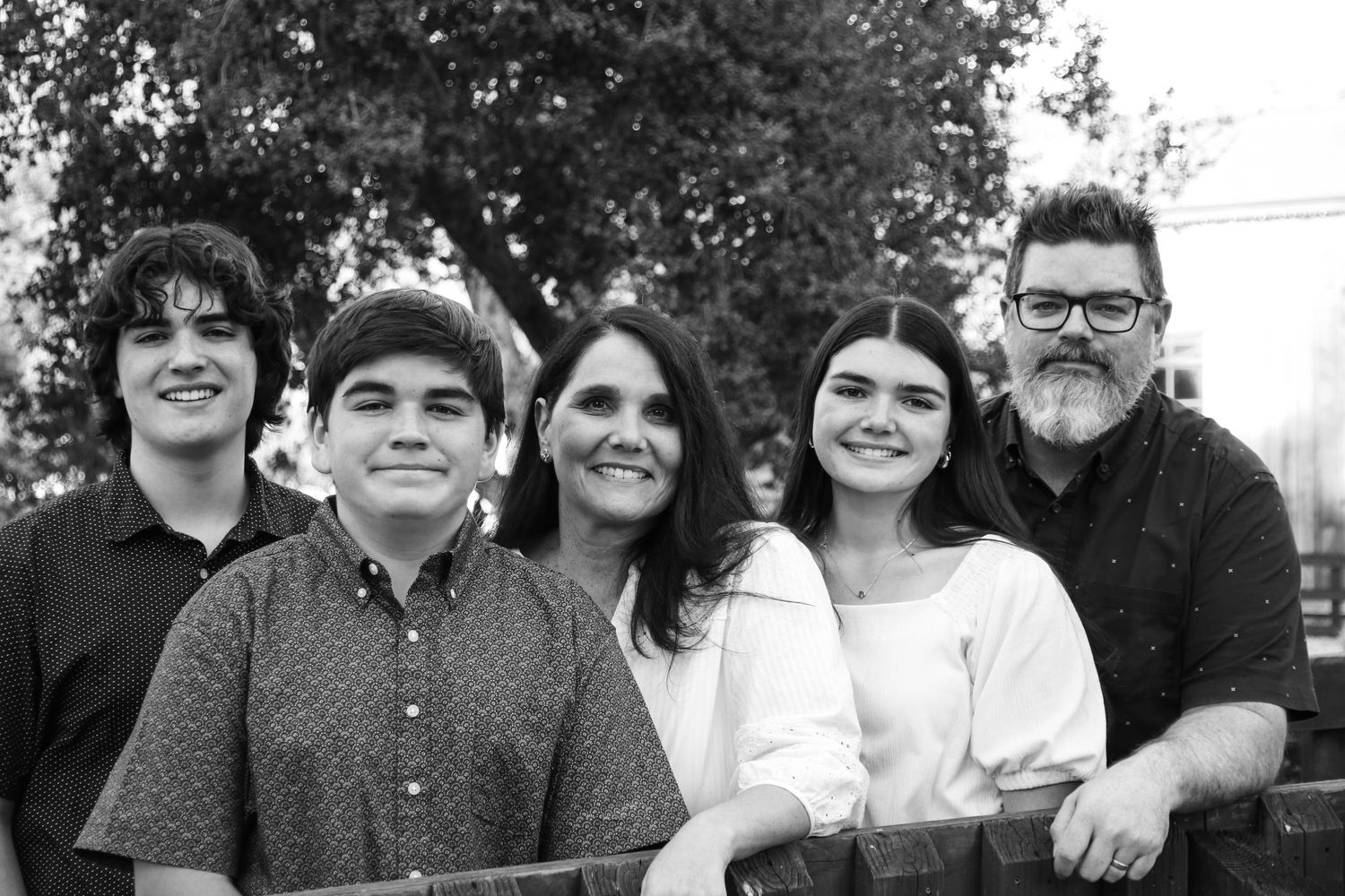 Casual family photo taken in an outdoor setting with trees and greenery.