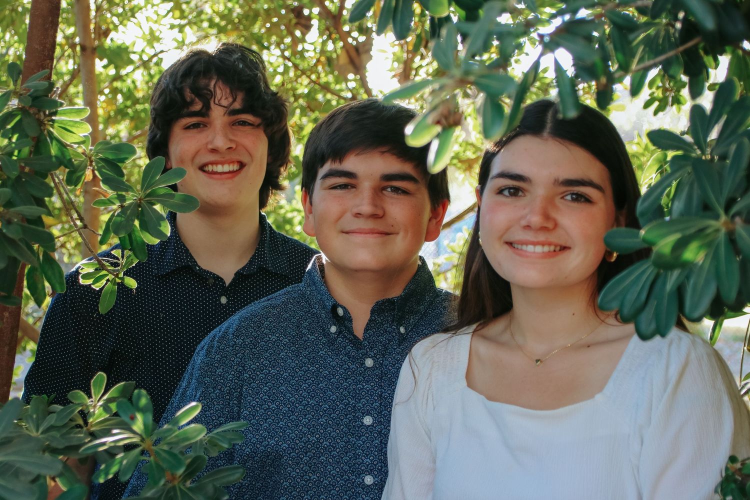 Three people sitting together and smiling under trees in both color and black and white shots.