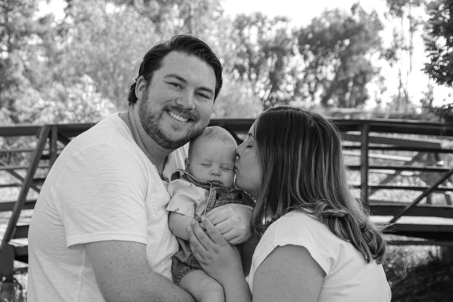 Family shares tender moments together in an outdoor setting with rustic wooden fence backdrop.
