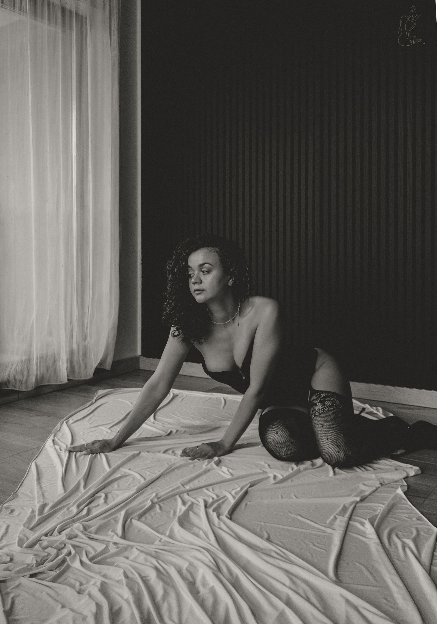 Black and white artistic photo of woman in black lingerie and stockings on white sheets.