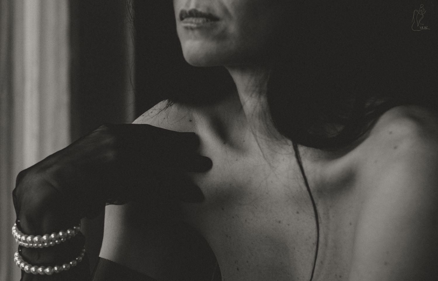 Black and white photo of a woman wearing pearl bracelets and gloves, showcasing elegant jewelry and bare shoulder.