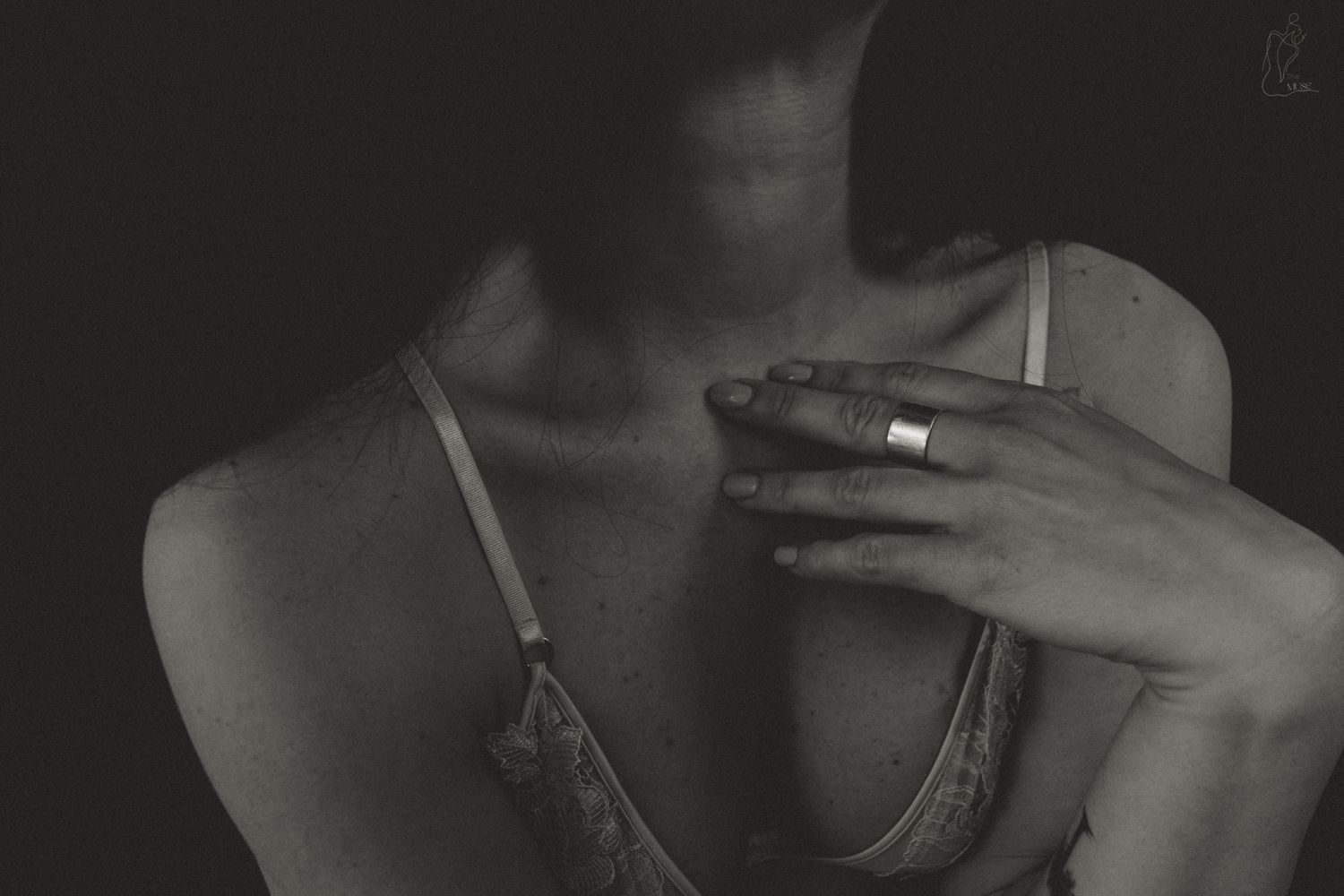 Black and white photo of a woman in a lace bra with a hand resting on her chest wearing a silver ring.
