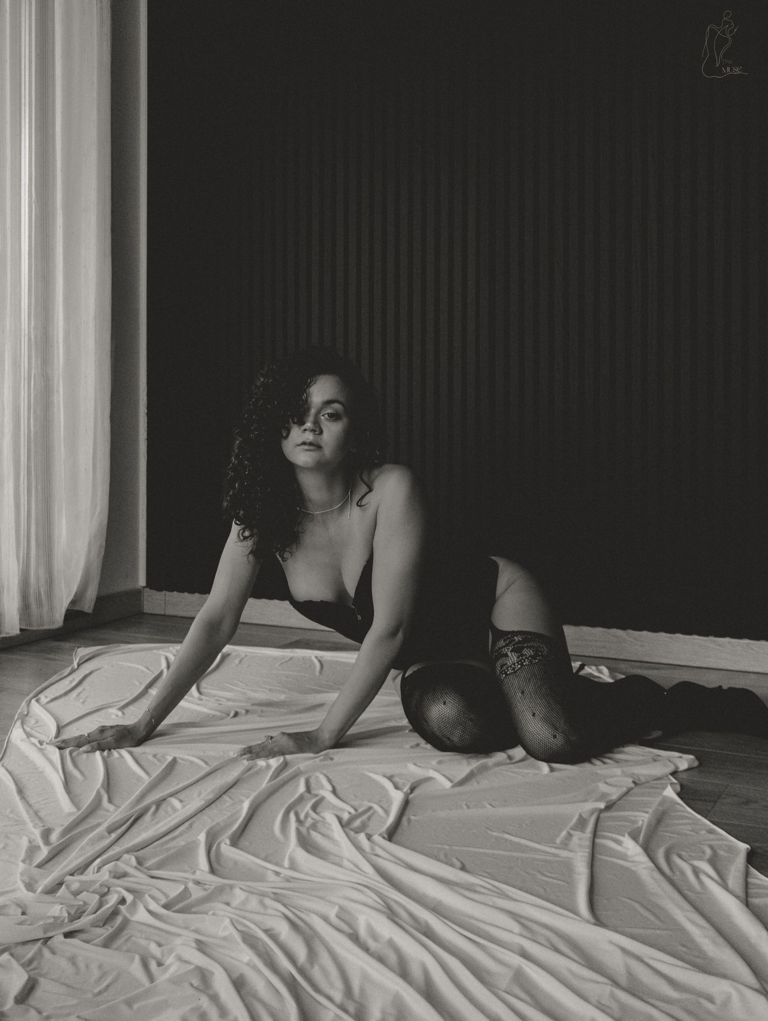 Black and white boudoir photo of woman in black lingerie posing on white draped fabric.