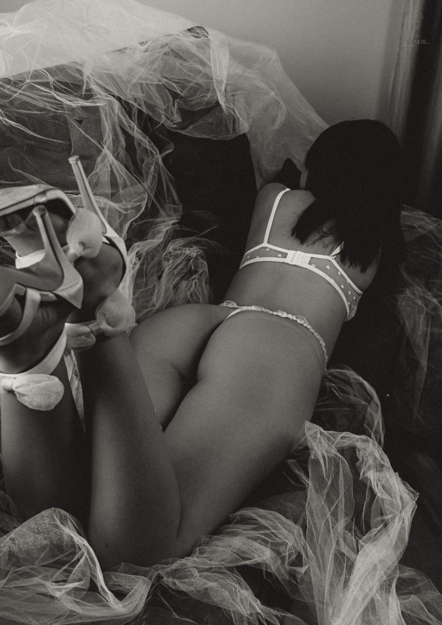 Black and white boudoir photo of a woman in white lingerie posed on fabric.