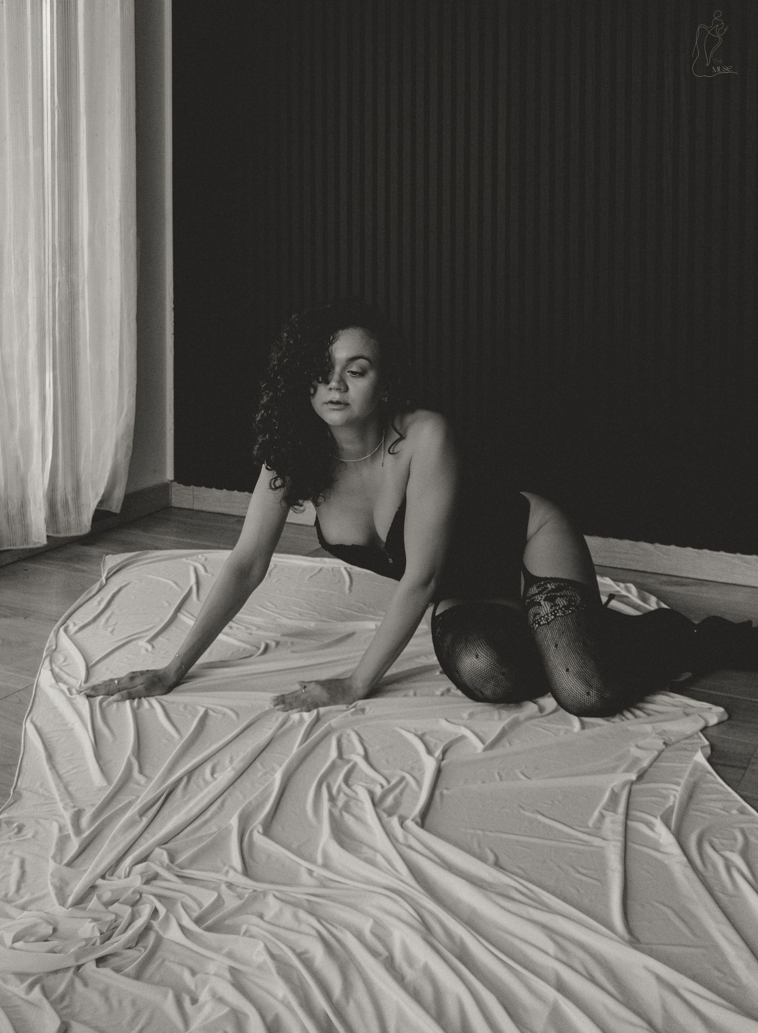 Black and white boudoir portrait of woman in lingerie reclining on draped white fabric.