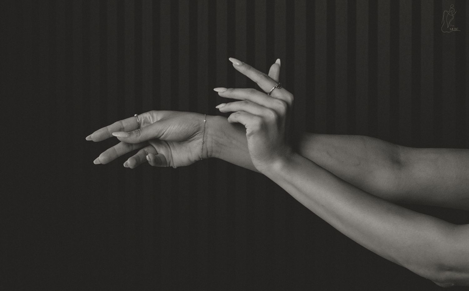Black and white artistic close-up of two graceful hands against a dark striped background.