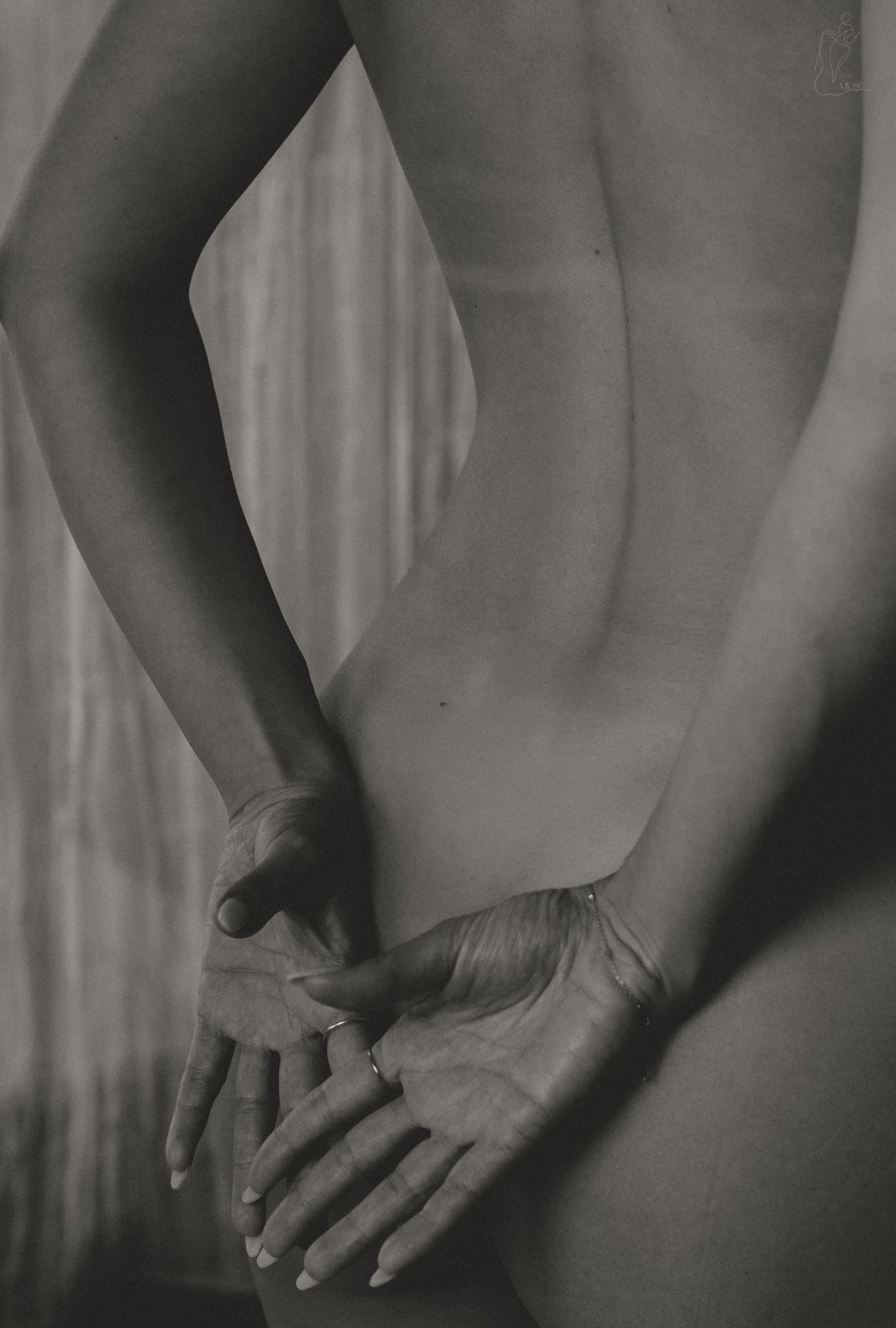 Black and white artistic close-up of a persons back with hands clasped behind them.