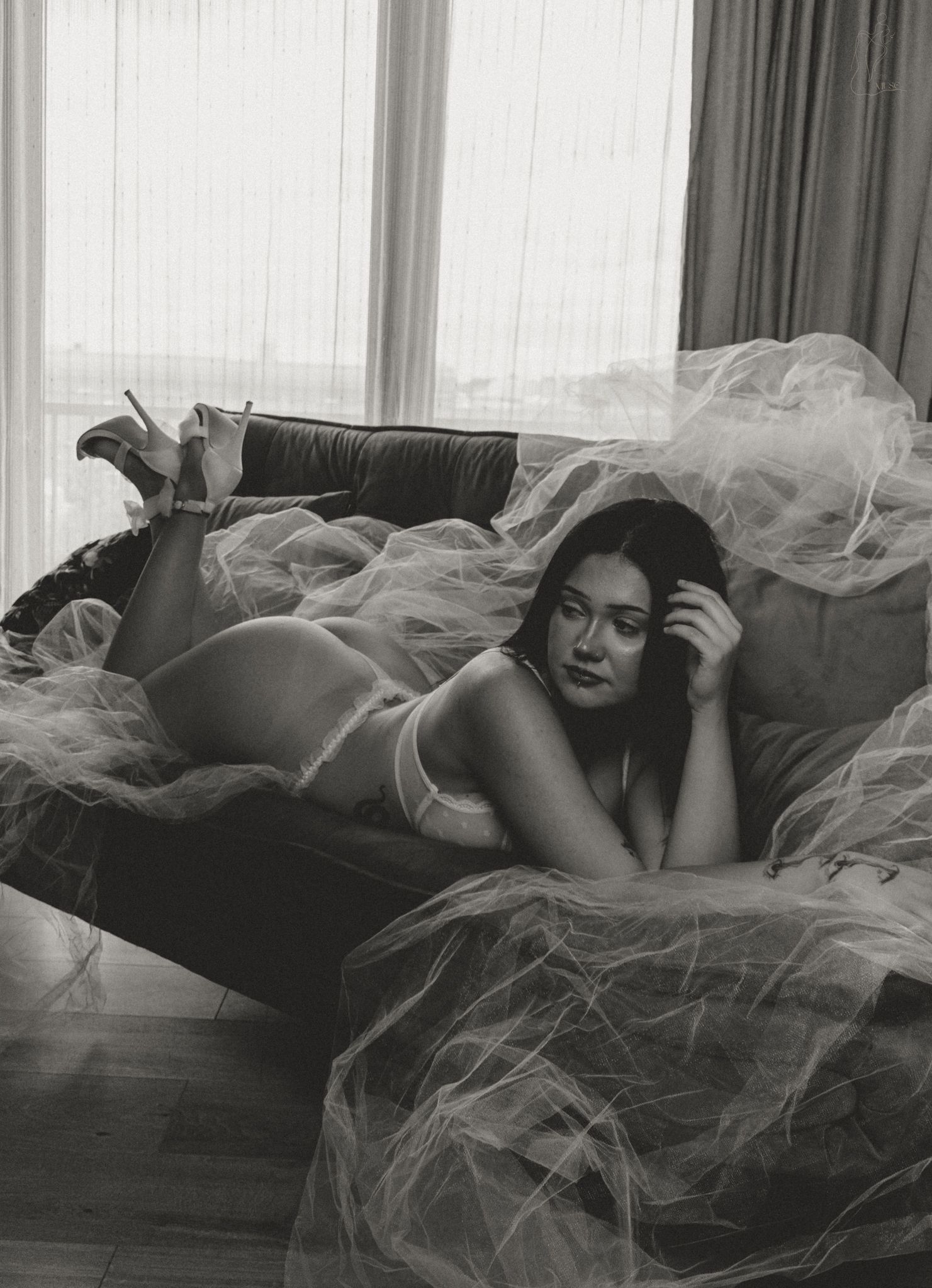 Black and white boudoir photo of a pregnant woman in lingerie lying on a sofa draped with tulle fabric.