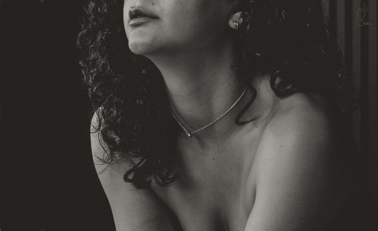 Close-up black and white portrait of woman with curly hair wearing a delicate chain necklace.