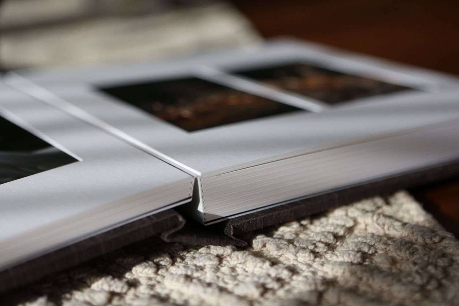 Close-up view of white photo album pages on a textured carpet showing partial polaroid photographs.