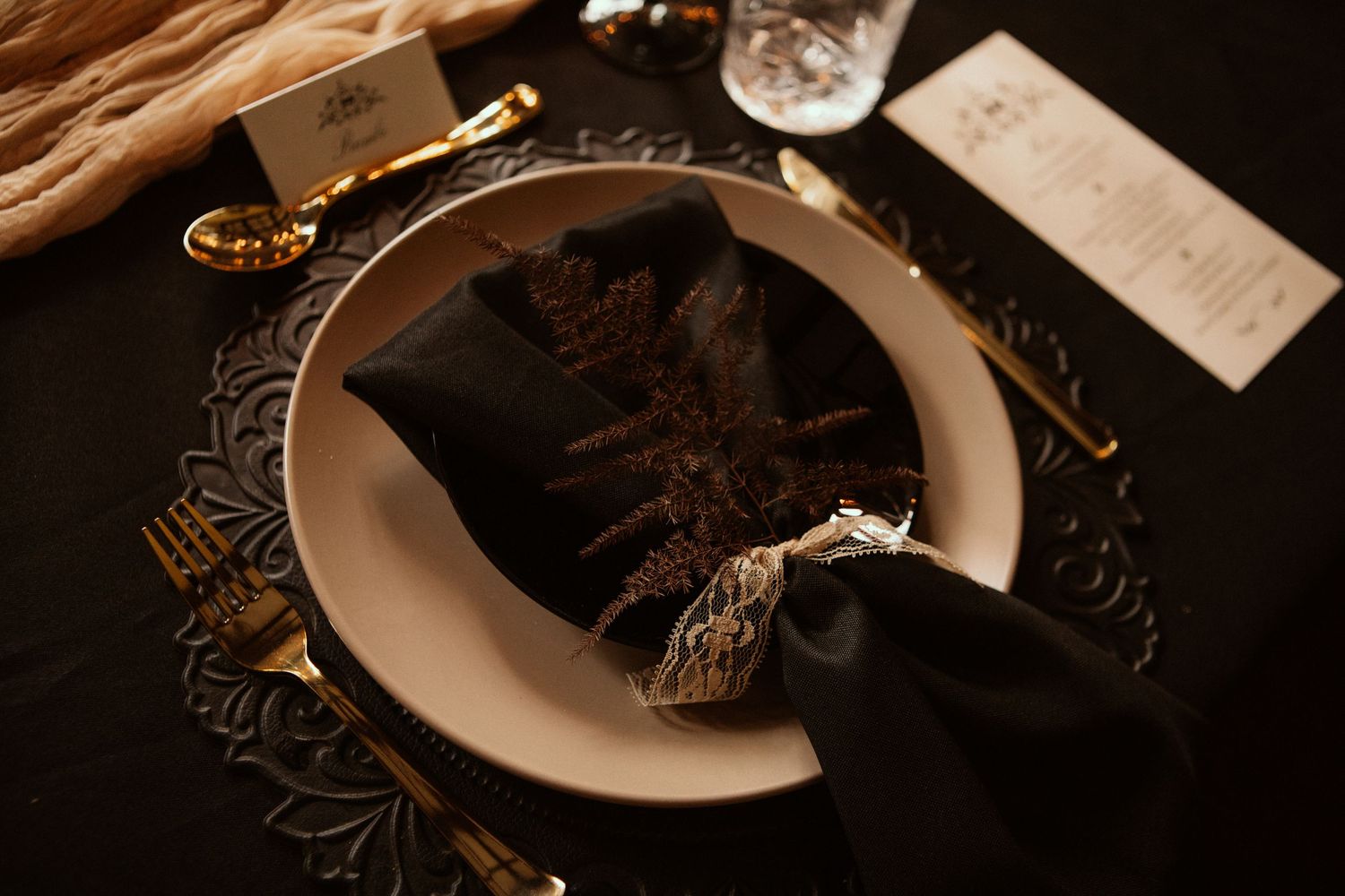 Elegant table setting with white plate and dark napkin against black tablecloth.