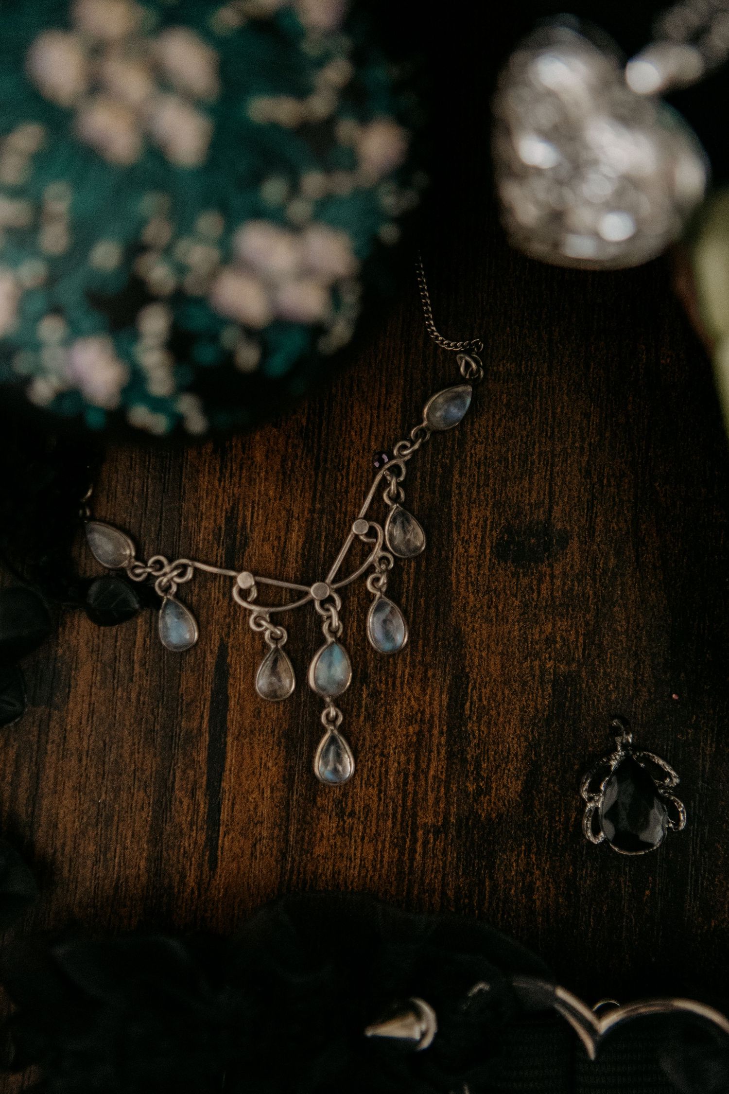 Silver chandelier necklace with moonstone teardrop pendants displayed on dark wood surface with rings and jewelry.