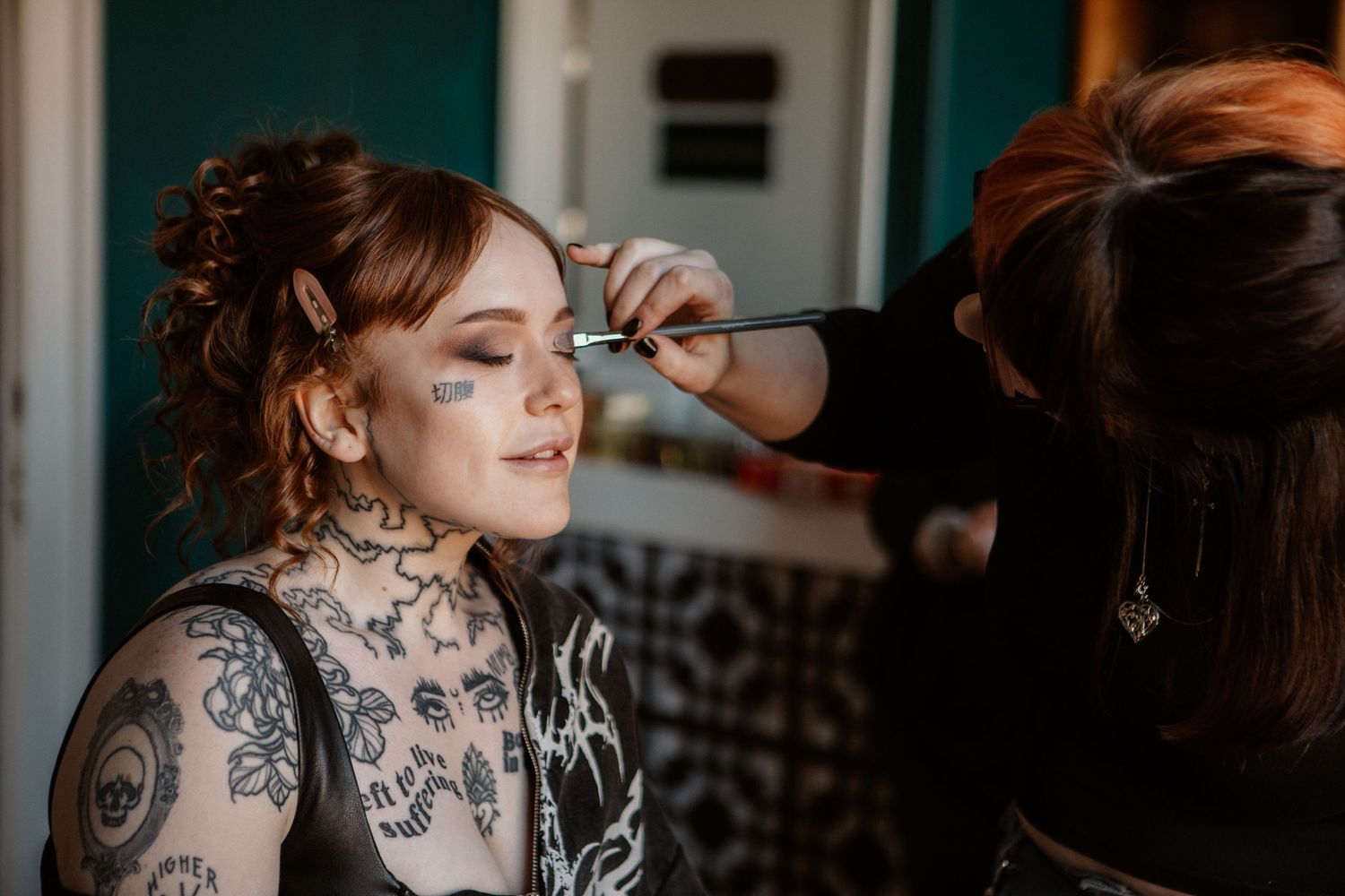Makeup artist applying eye makeup to a heavily tattooed redhead bride with face tattoos.