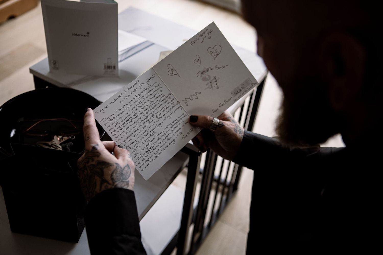 Person reading a handwritten letter with drawings, holding it near a black box on a wooden table.