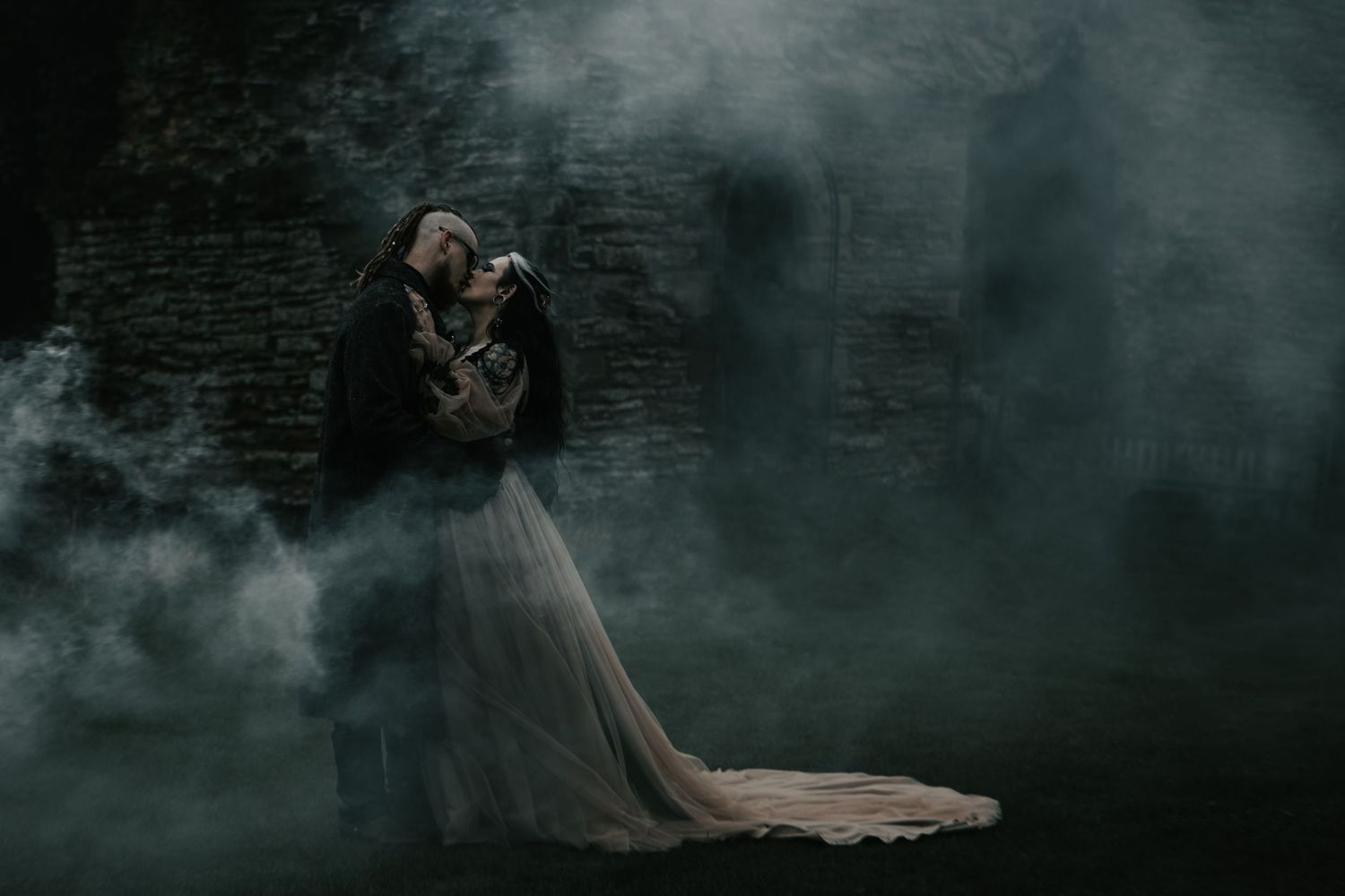 A couple embraces in a dramatic, misty dark setting, with the woman in a flowing white gown and man in a dark cape.