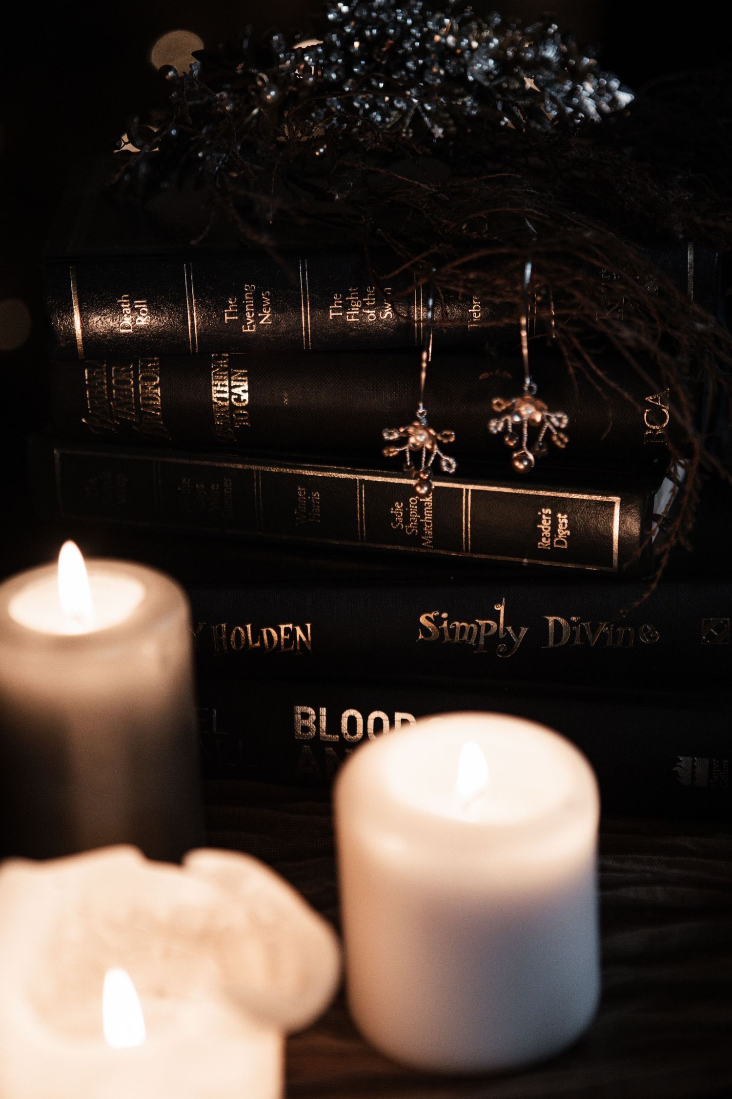 Close-up of dark gothic books including Simply Divine and Blood with glowing candles and jewelry.