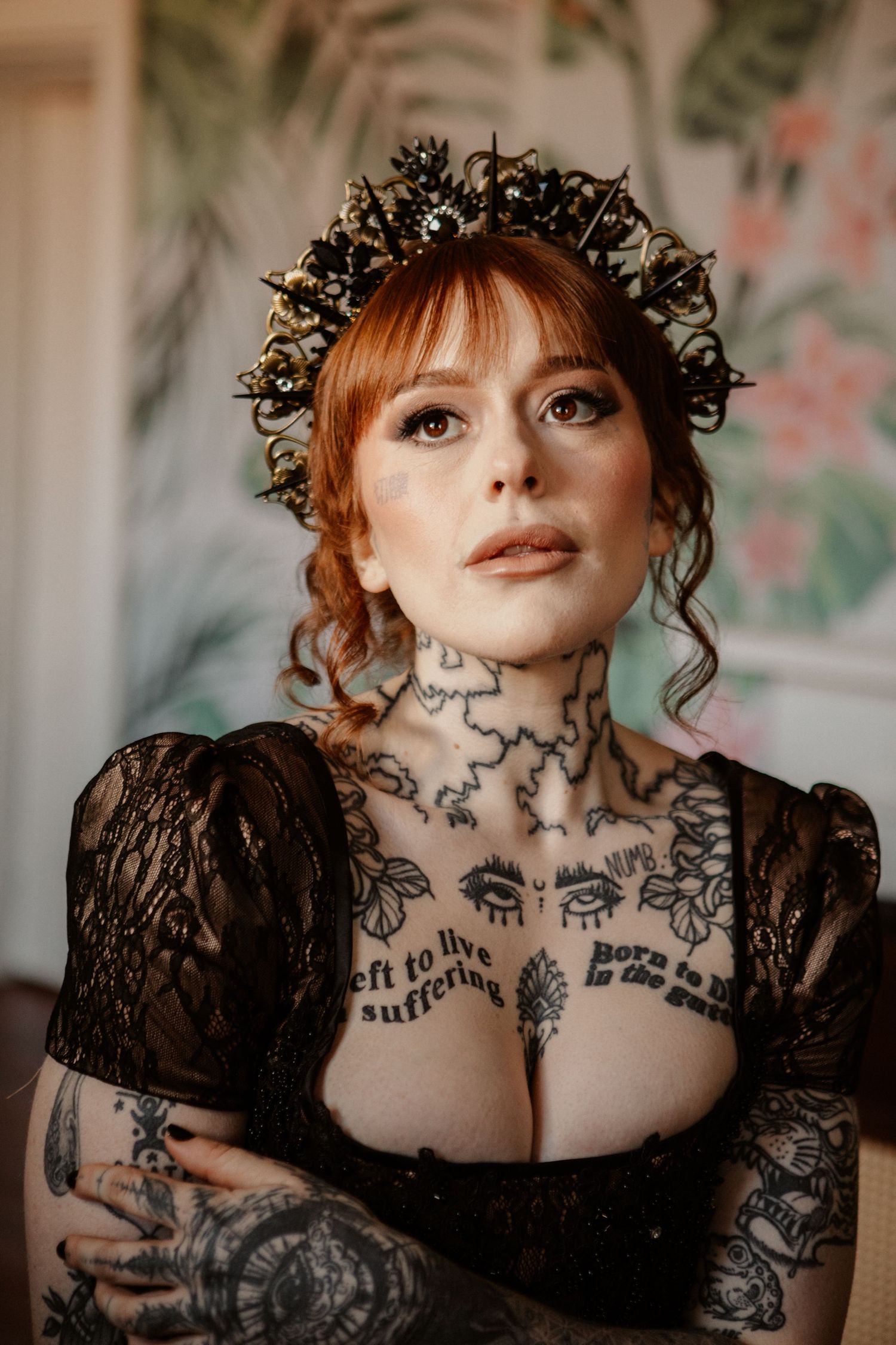 Tattooed redhead bride in black lace dress wearing elaborate dark crown with gold embellishments.