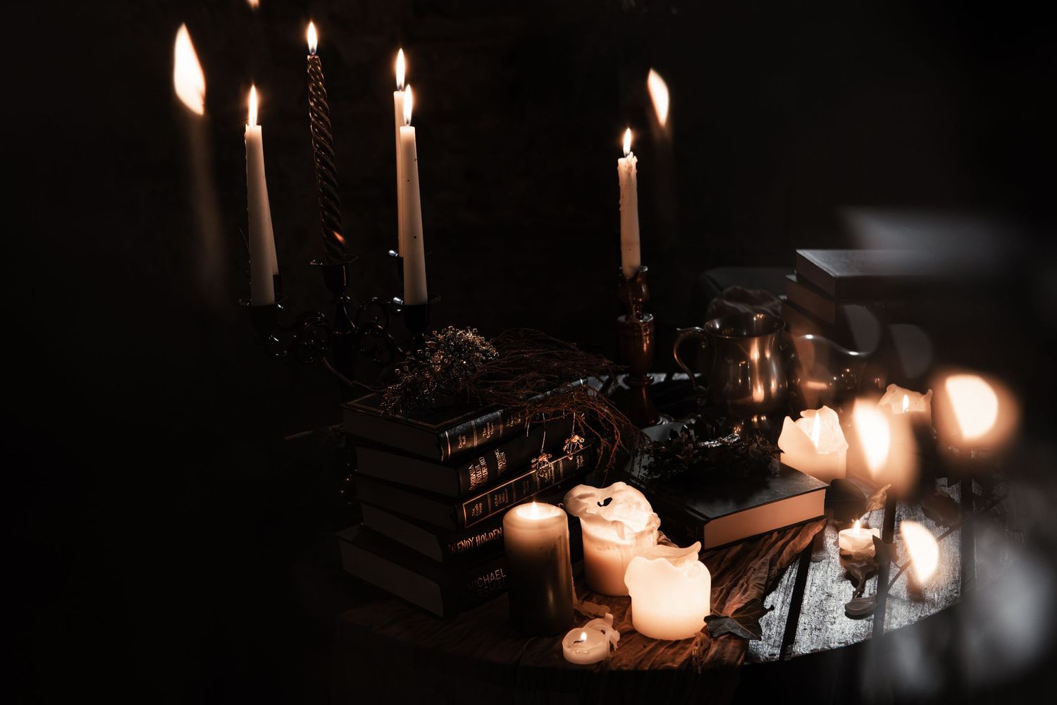 Gothic candlelit altar with tall taper candles, dark books, and decorative objects in moody lighting.