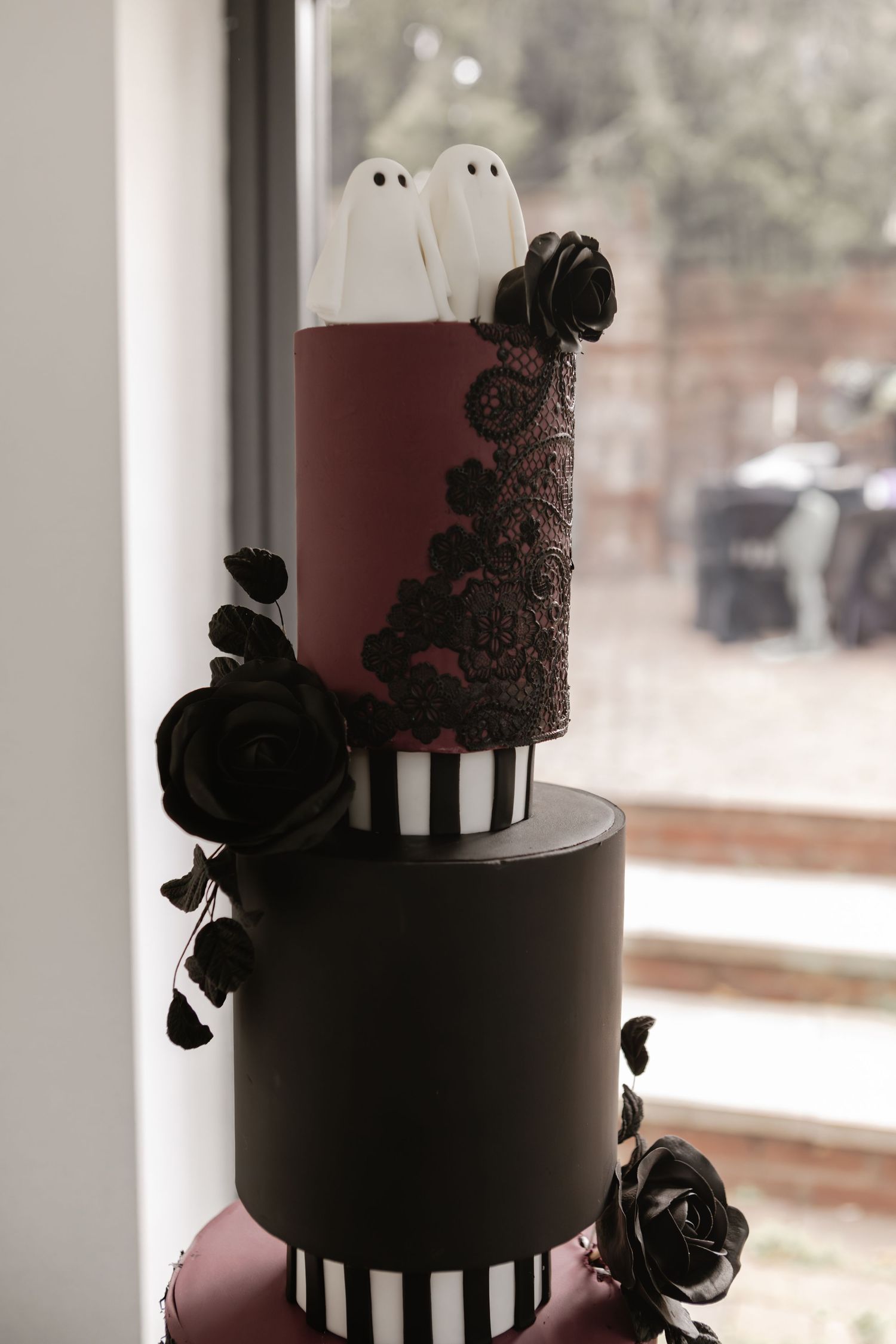 Gothic Halloween wedding cake with white ghost toppers, black roses, dark lace details, and black and white striped tier.