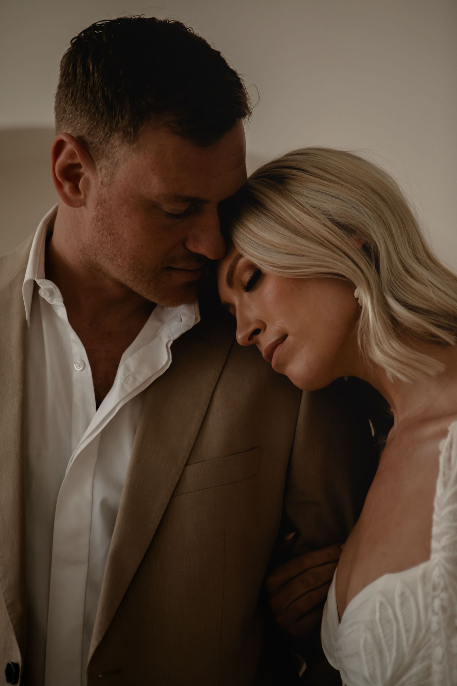 Intimate romantic portrait of a couple in warm lighting, with her leaning on his shoulder in a tender embrace.