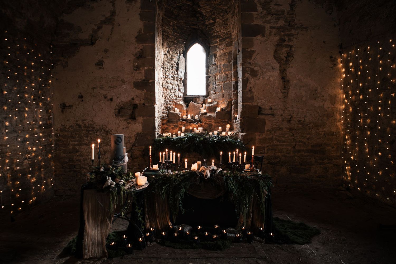 Atmospheric gothic wedding reception space with fairy lights, candles, and dark floral altar in stone ruins.