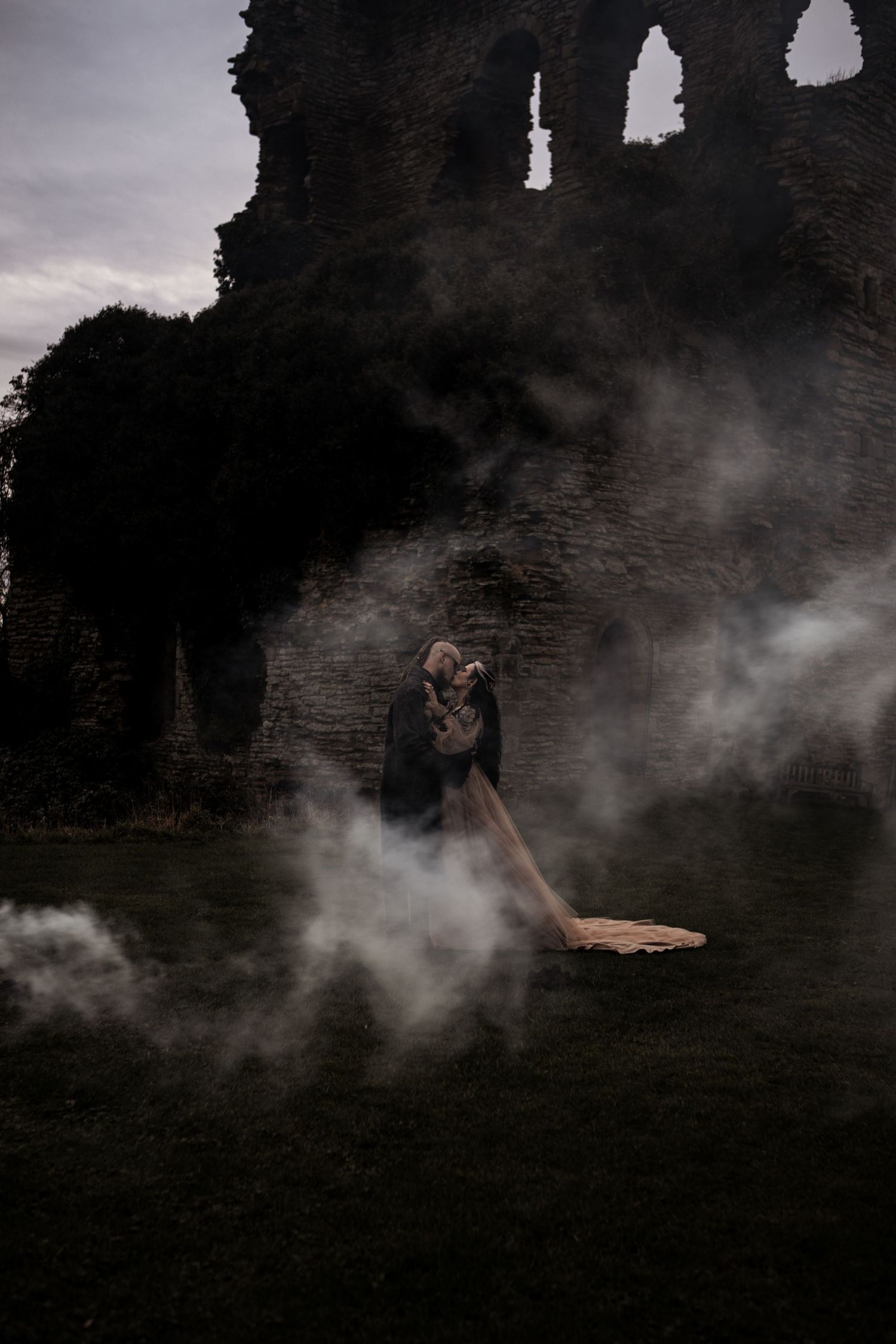 Couple embracing amid smoke at ancient stone ruins during a moody outdoor wedding shoot.