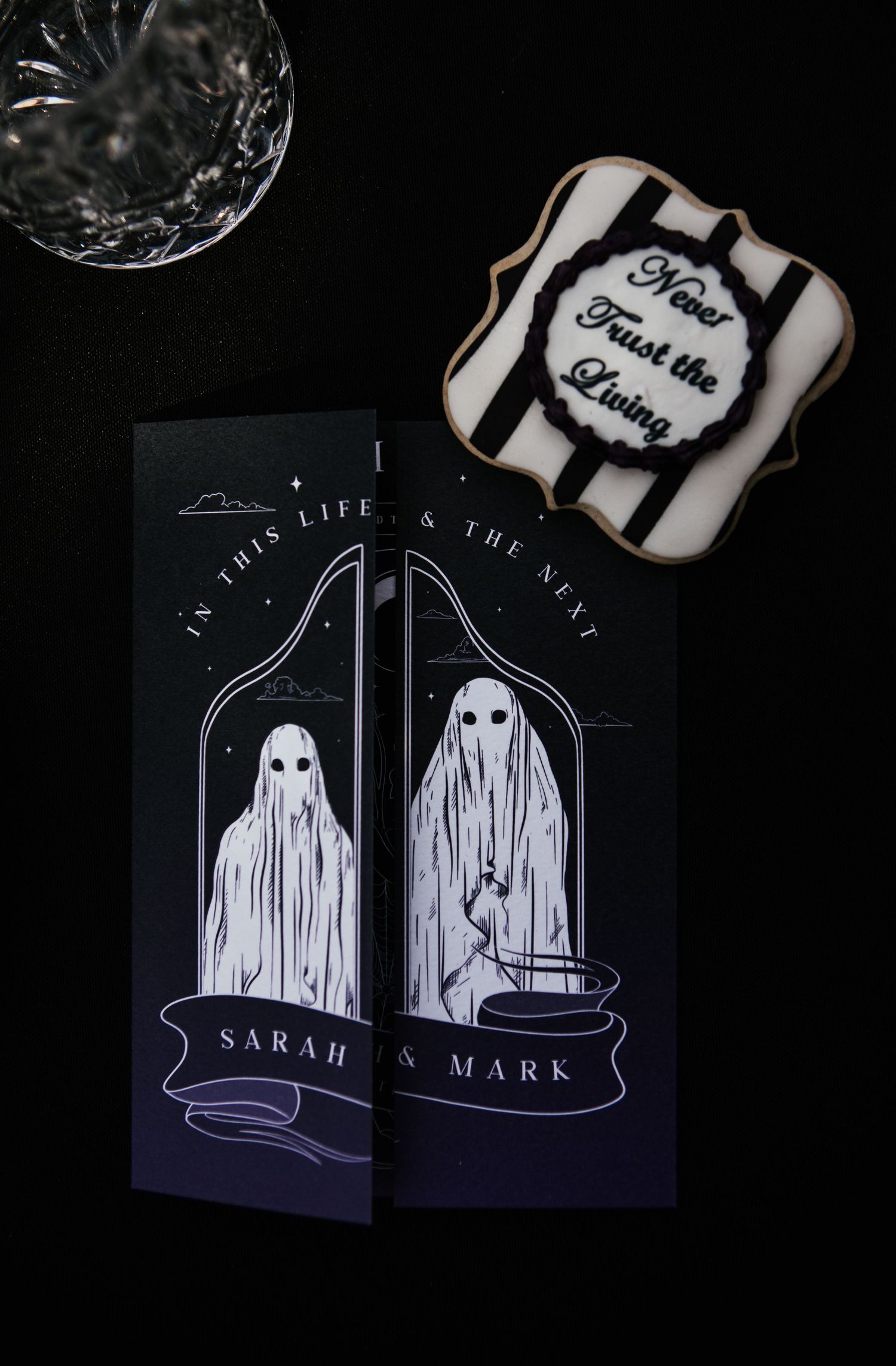 Gothic wedding stationery with ghost illustrations reading In This Life & The Next for Sarah & Mark beside a Never Trust the Living cookie.