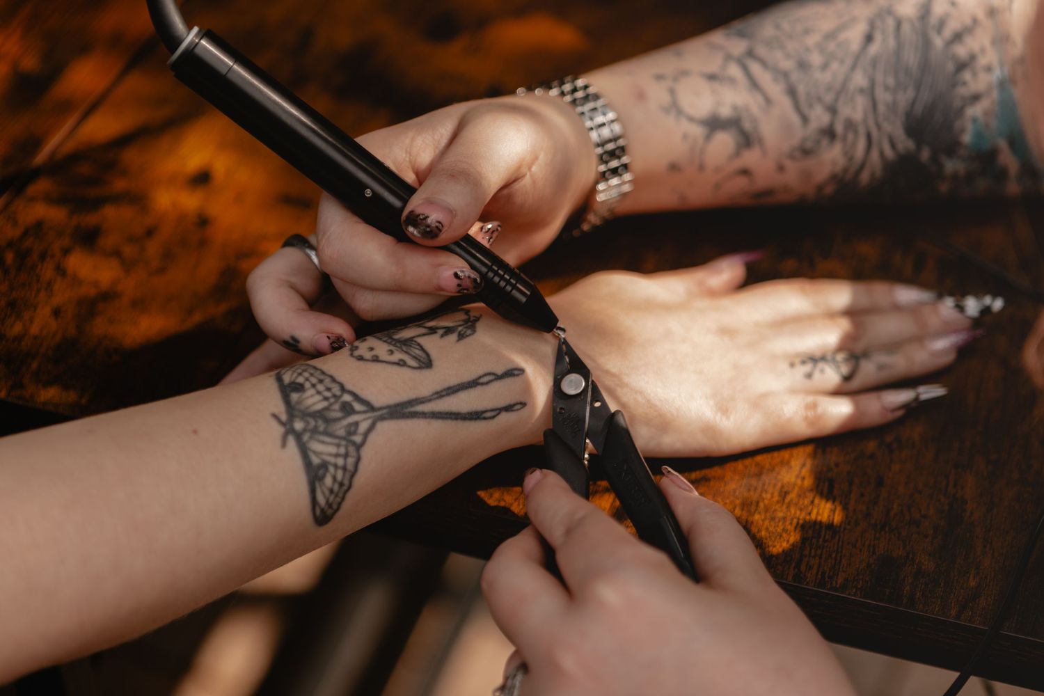 Tattoo artist drawing a butterfly design on a client's wrist with a tattoo machine in a studio.