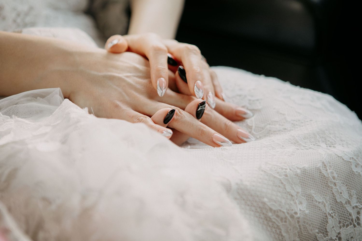 Close up of hands with black nail polish resting on white lace fabric.