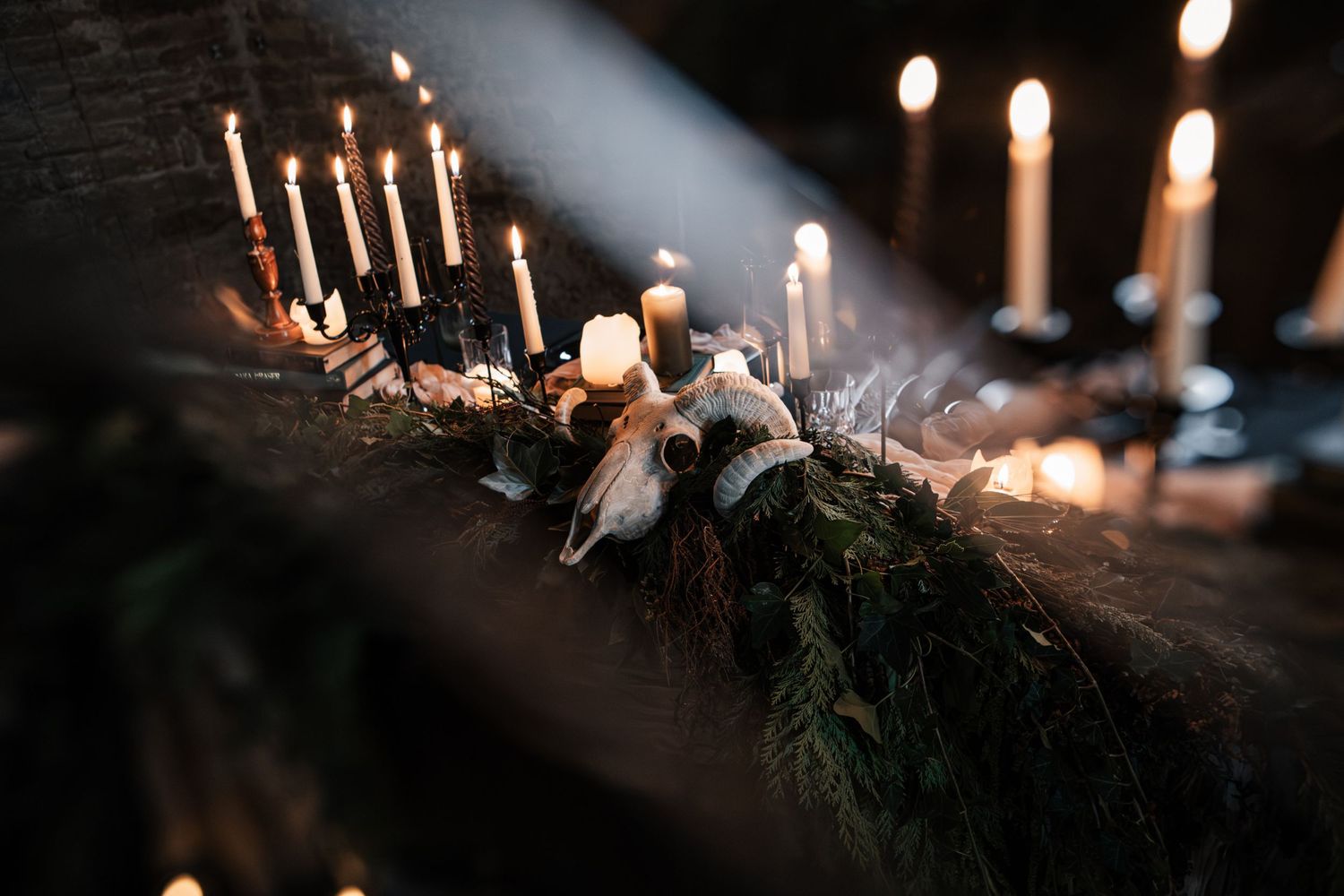 Dramatic gothic wedding tablescape with lit candles, animal skulls, and greenery in dark setting.