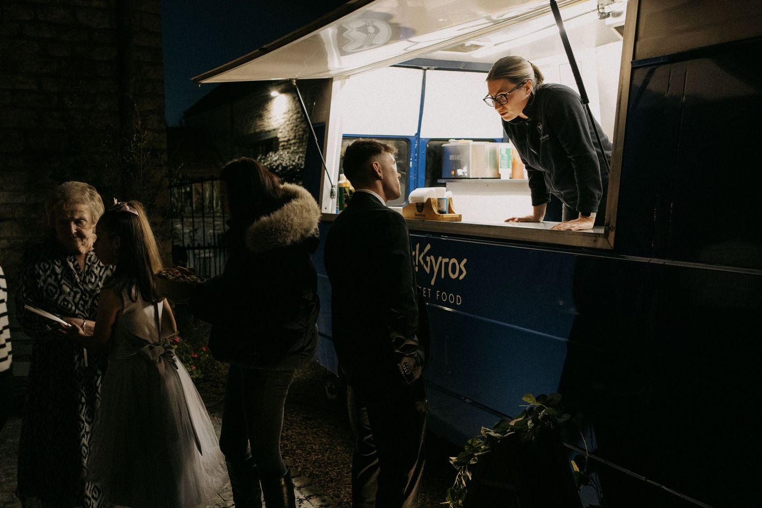 Guests ordering from a Kyros food truck at a dark outdoor wedding reception event.
