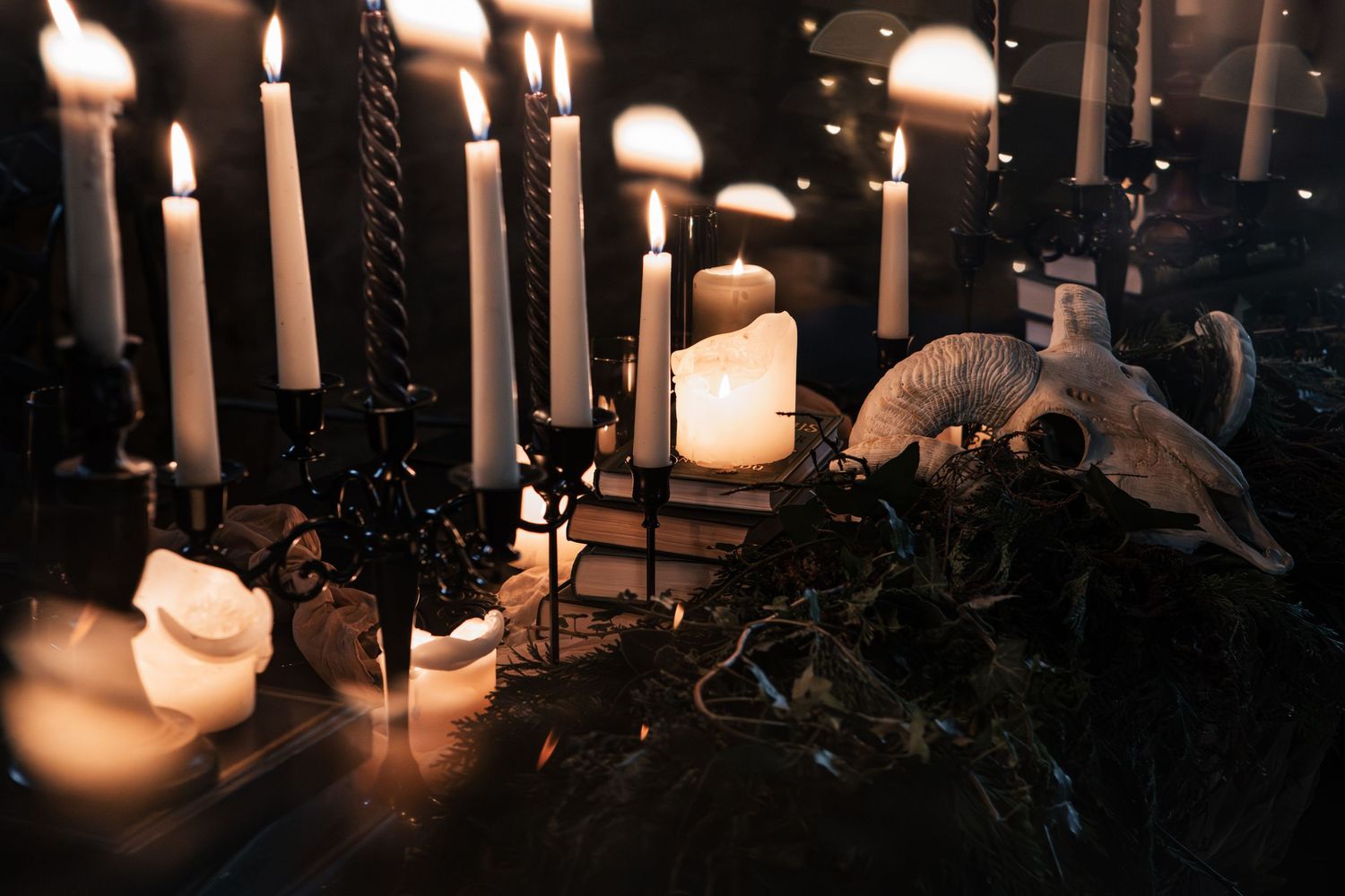 Dramatic gothic candlelit display with black candelabras, ram skull, and greenery in dark atmospheric setting.