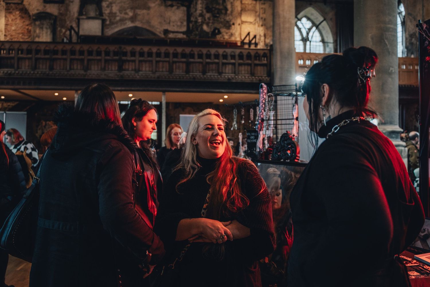 A group of people chatting in dark moody lighting with red tones at what appears to be a historic venue or church.