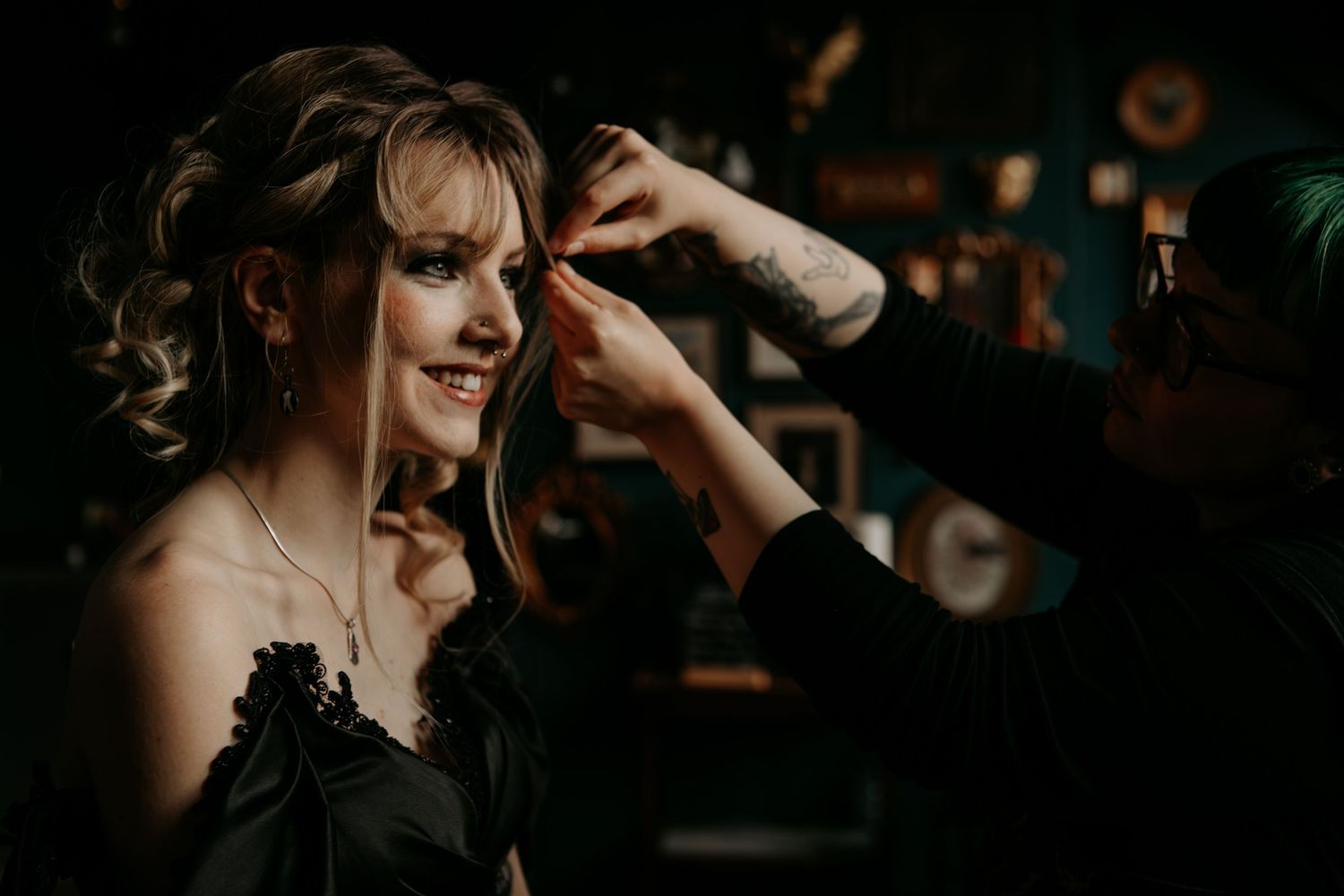 Individual wearing a black top having makeup applied in a dark moody setting with warm ambient lighting.